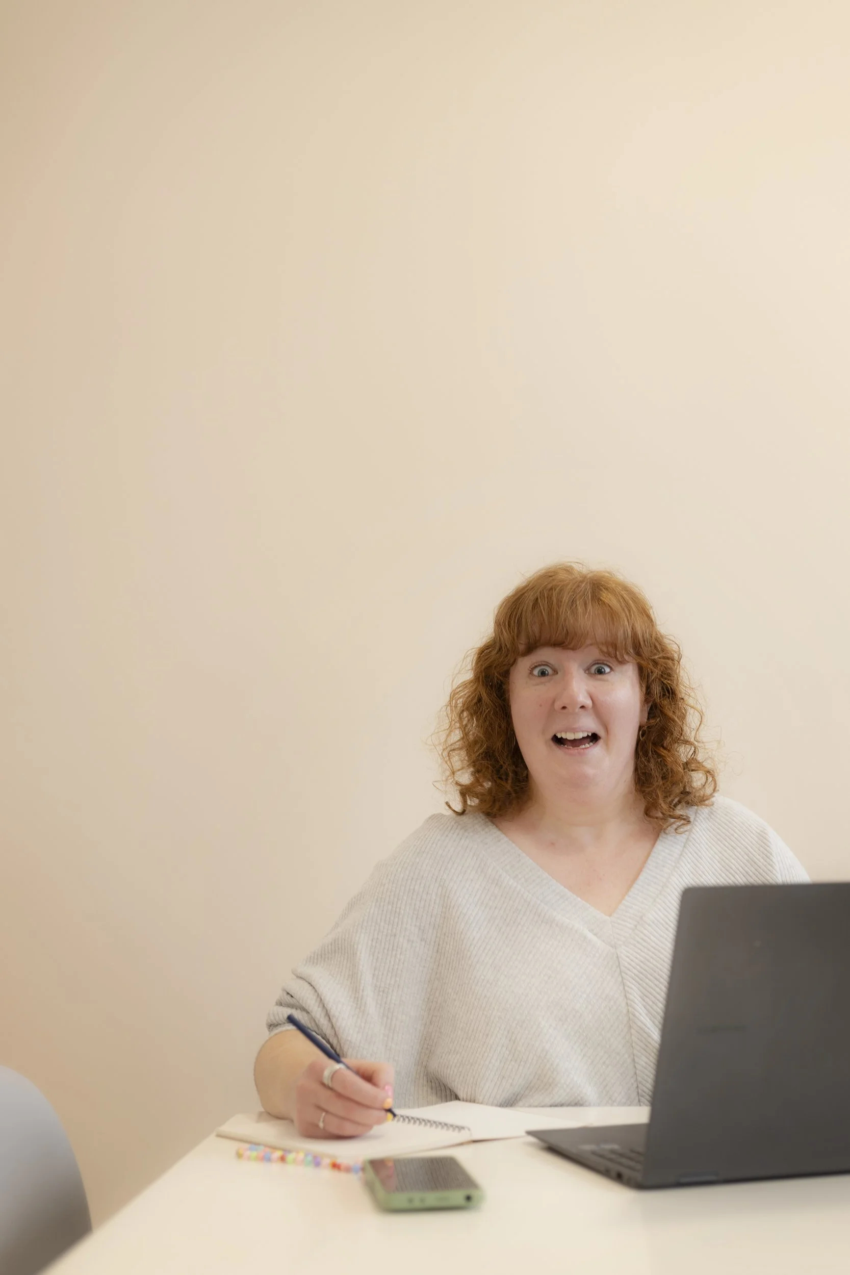 A woman sat at a desk pulling a funny face, as if shocked.