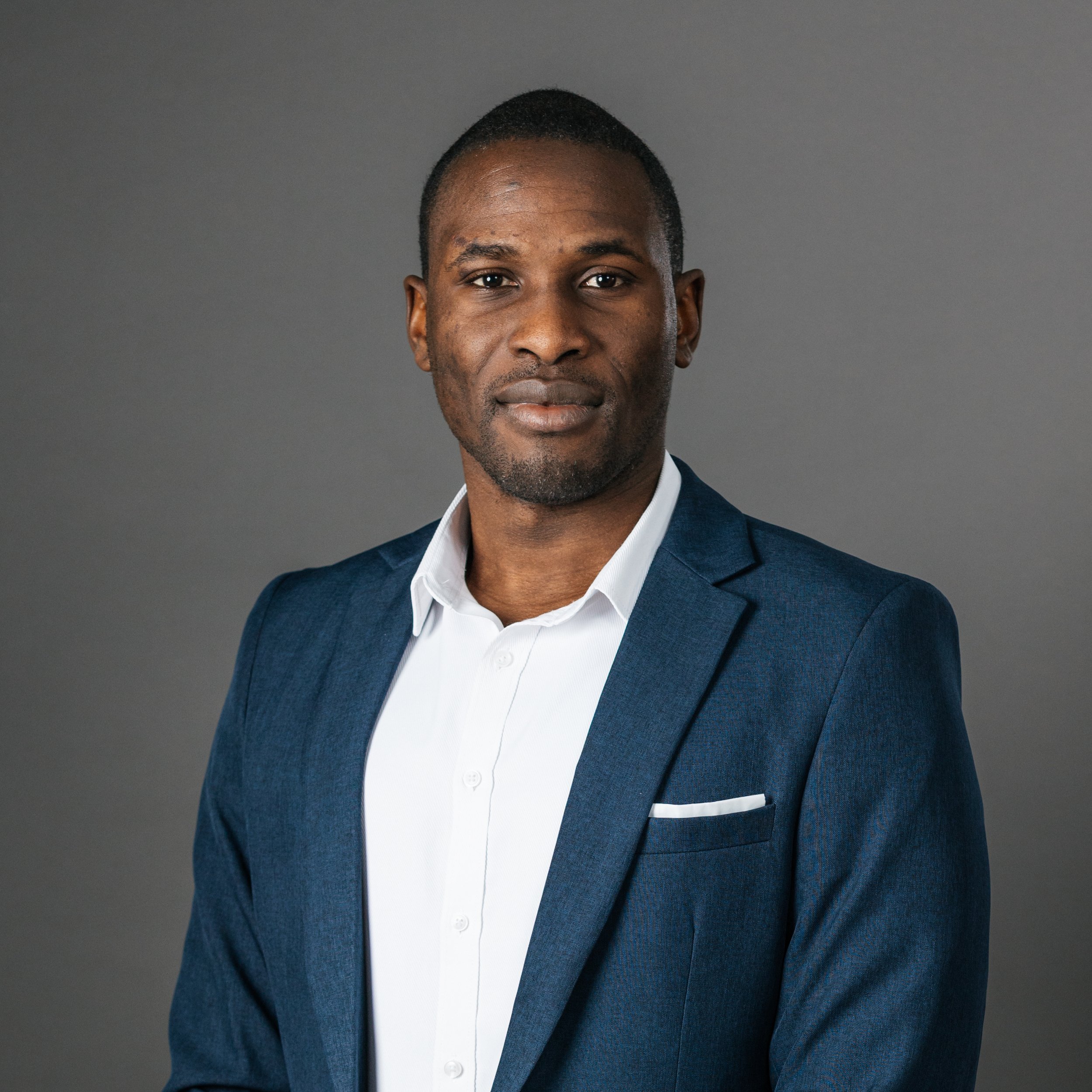 Man in a blue suit with white shirt against a gray background.