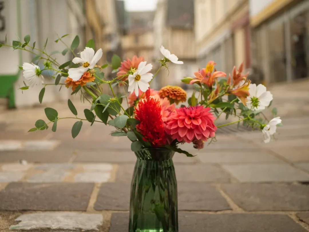 Un bouquet de fleurs colorées dans un vase vert sur un sol en pierre à l'extérieur.