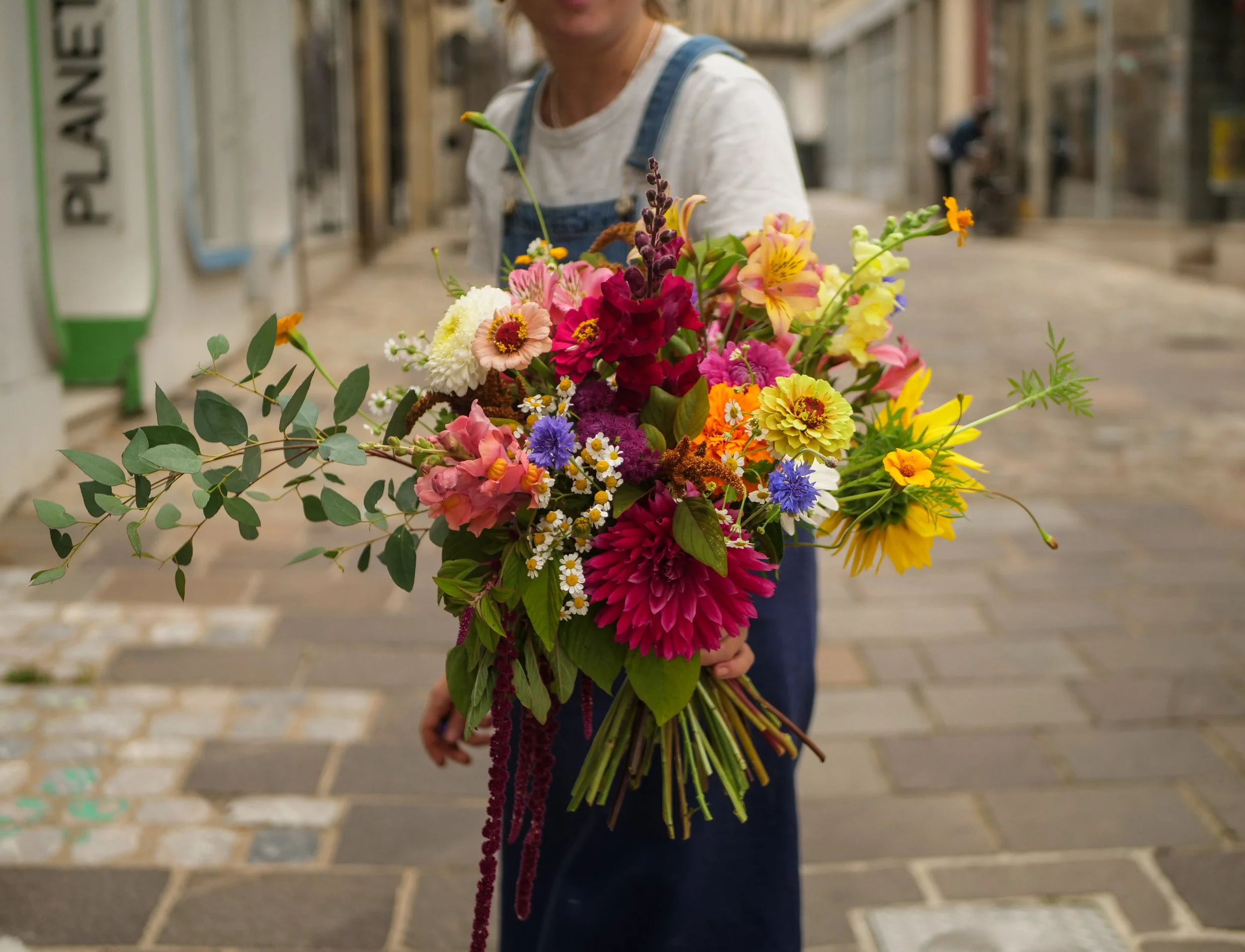 Personne tenant un bouquet de fleurs colorées dans une rue pavée.