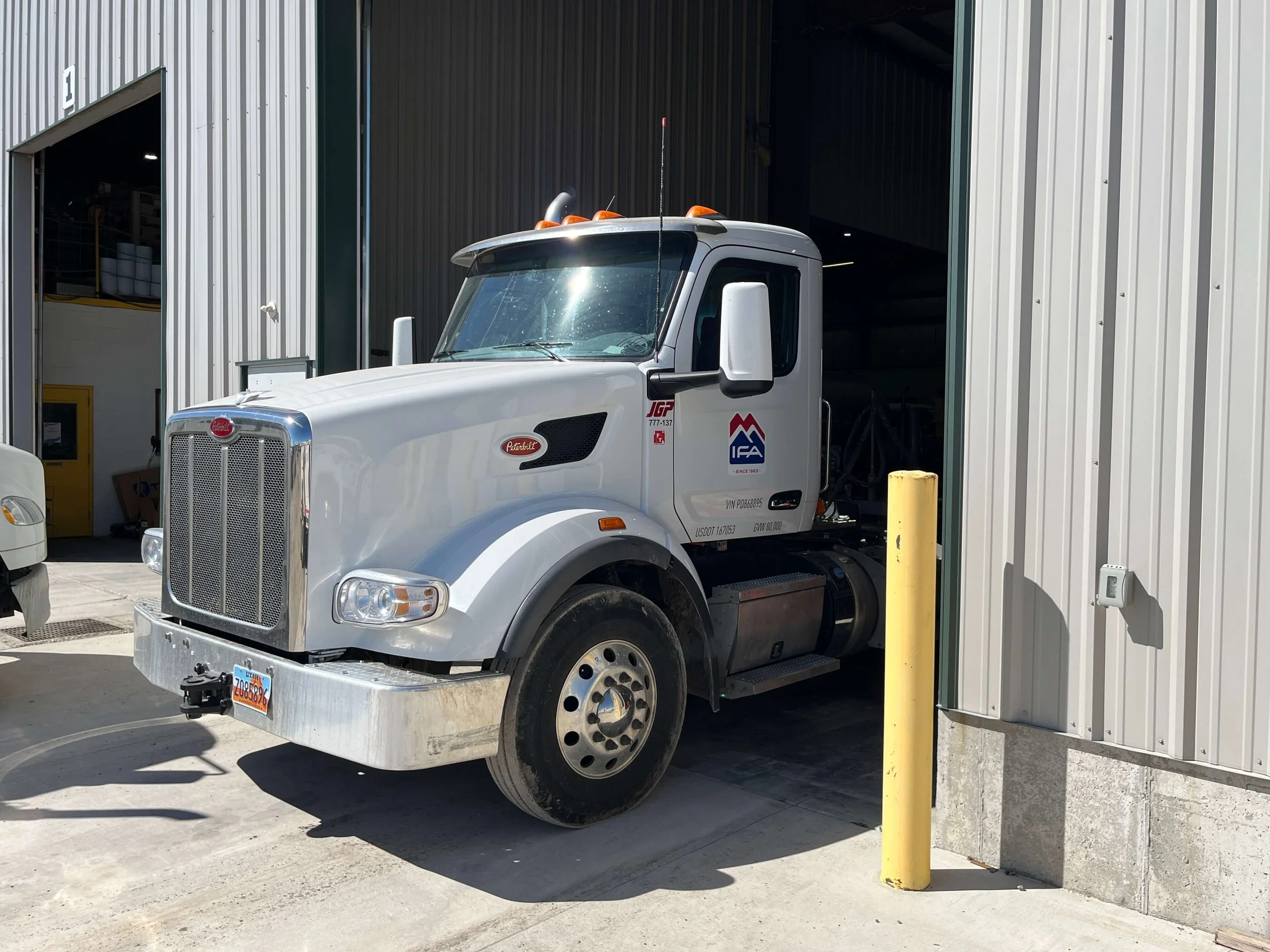 A white Peterbilt truck parked in front of an industrial building with an open garage door.