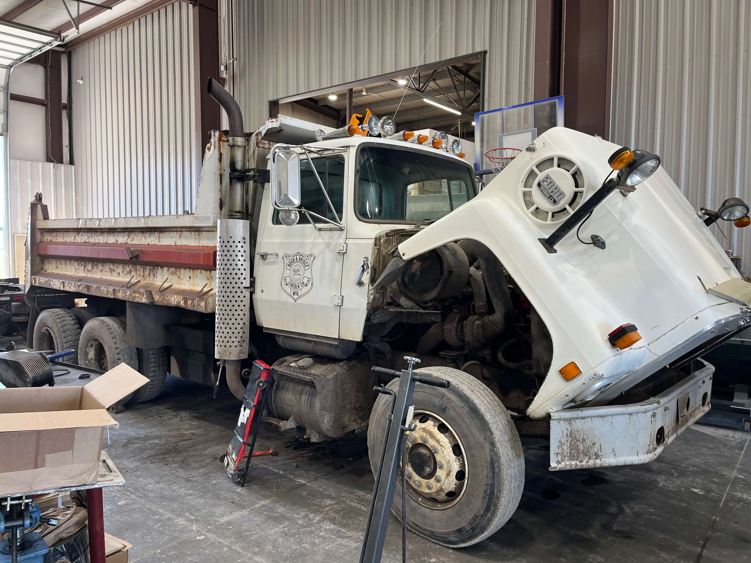 A white dump truck with its hood open in a garage setting.