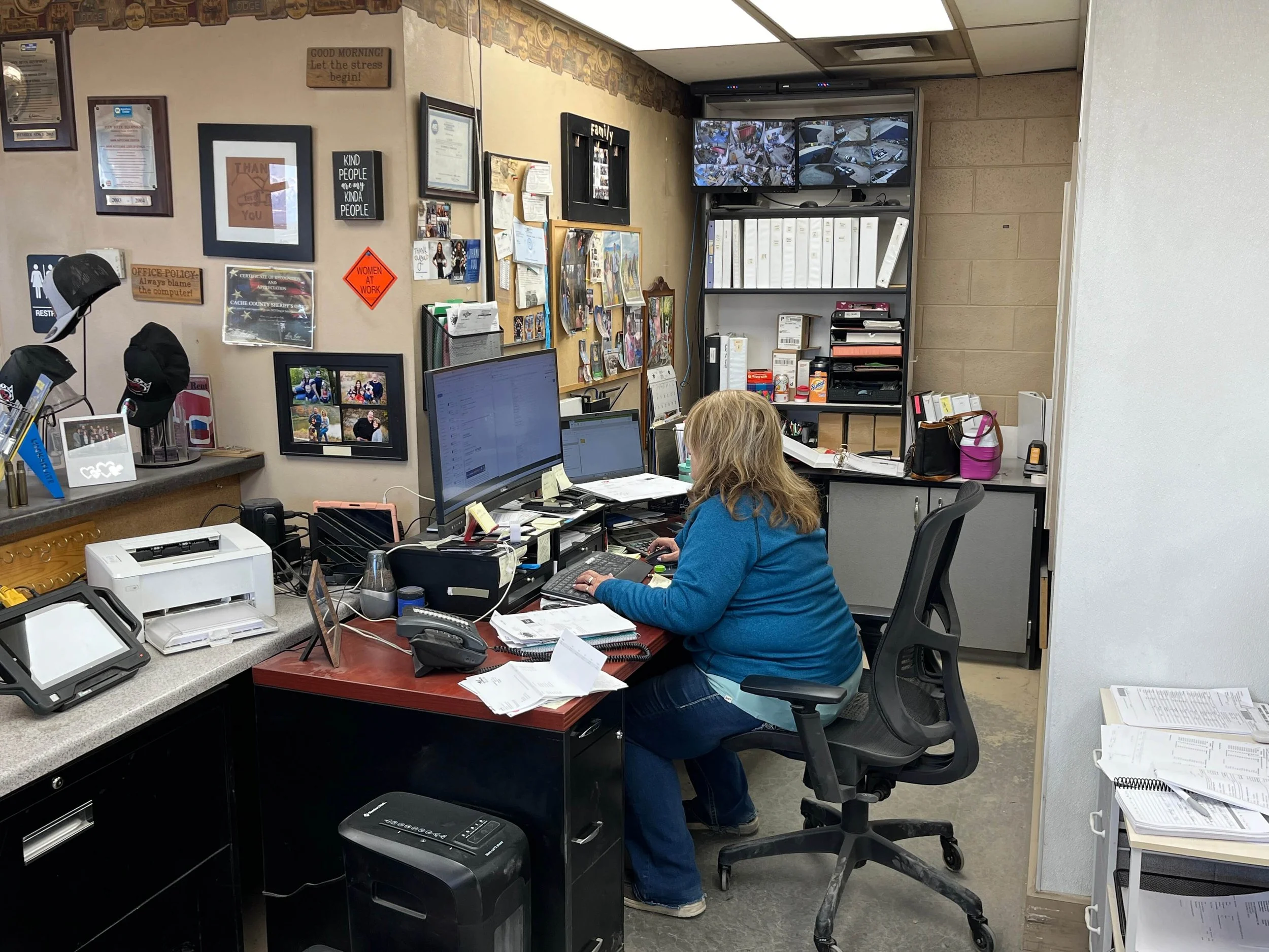 Office with Sherylee Black working at a desk, computer monitors, printer, and shelves with binders and files.