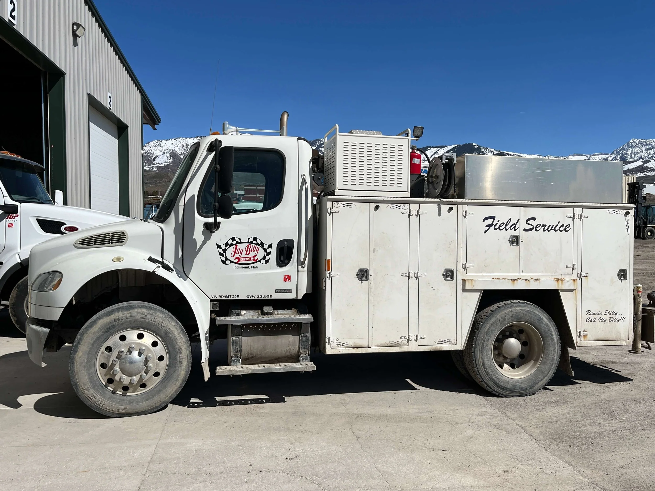 White field service truck parked in front of a garage with mountains in the background.