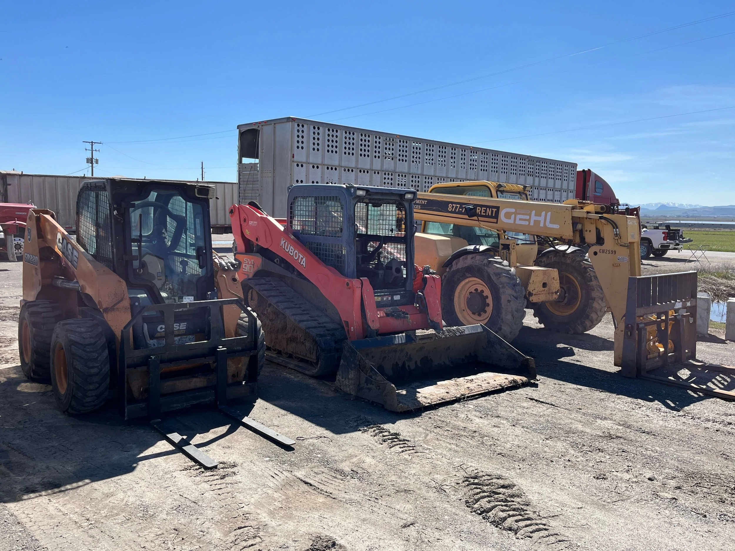 Construction site with three skid steer loaders and a forklift attachment.
