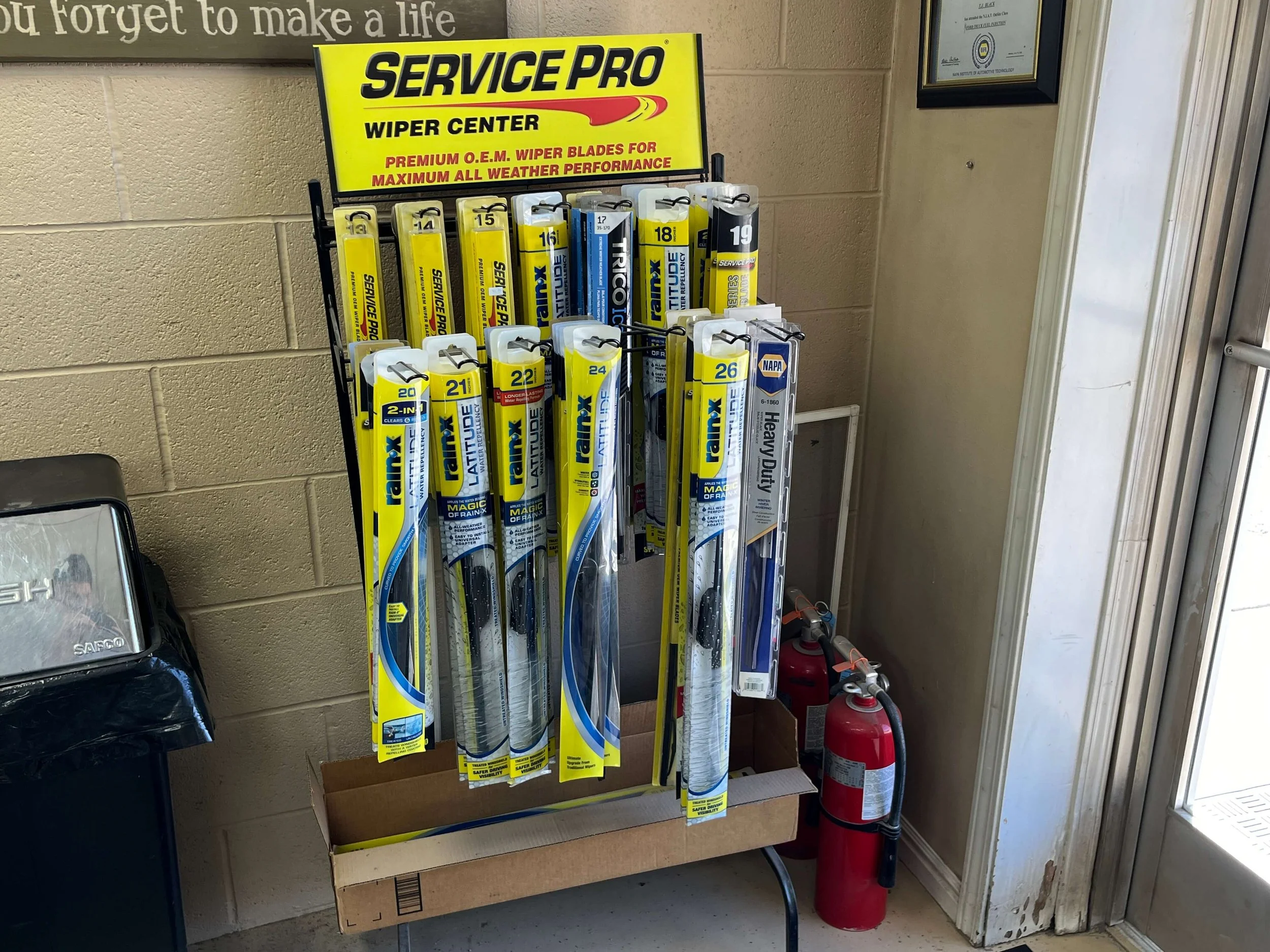 Display rack with various Rain-X and Service Pro wiper blades in a shop corner, next to a trash can and two fire extinguishers.
