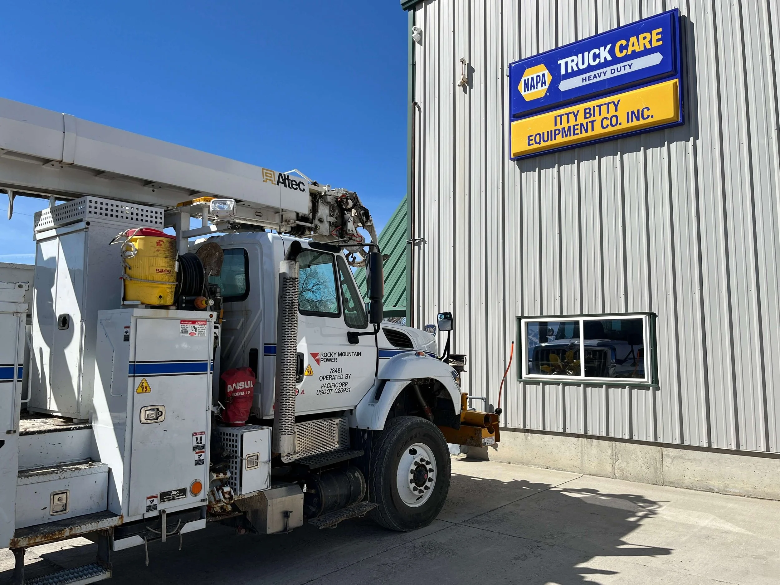 Utility truck parked outside a building with "NAPA Truck Care" and "Itty Bitty Equipment Co. Inc." signage.