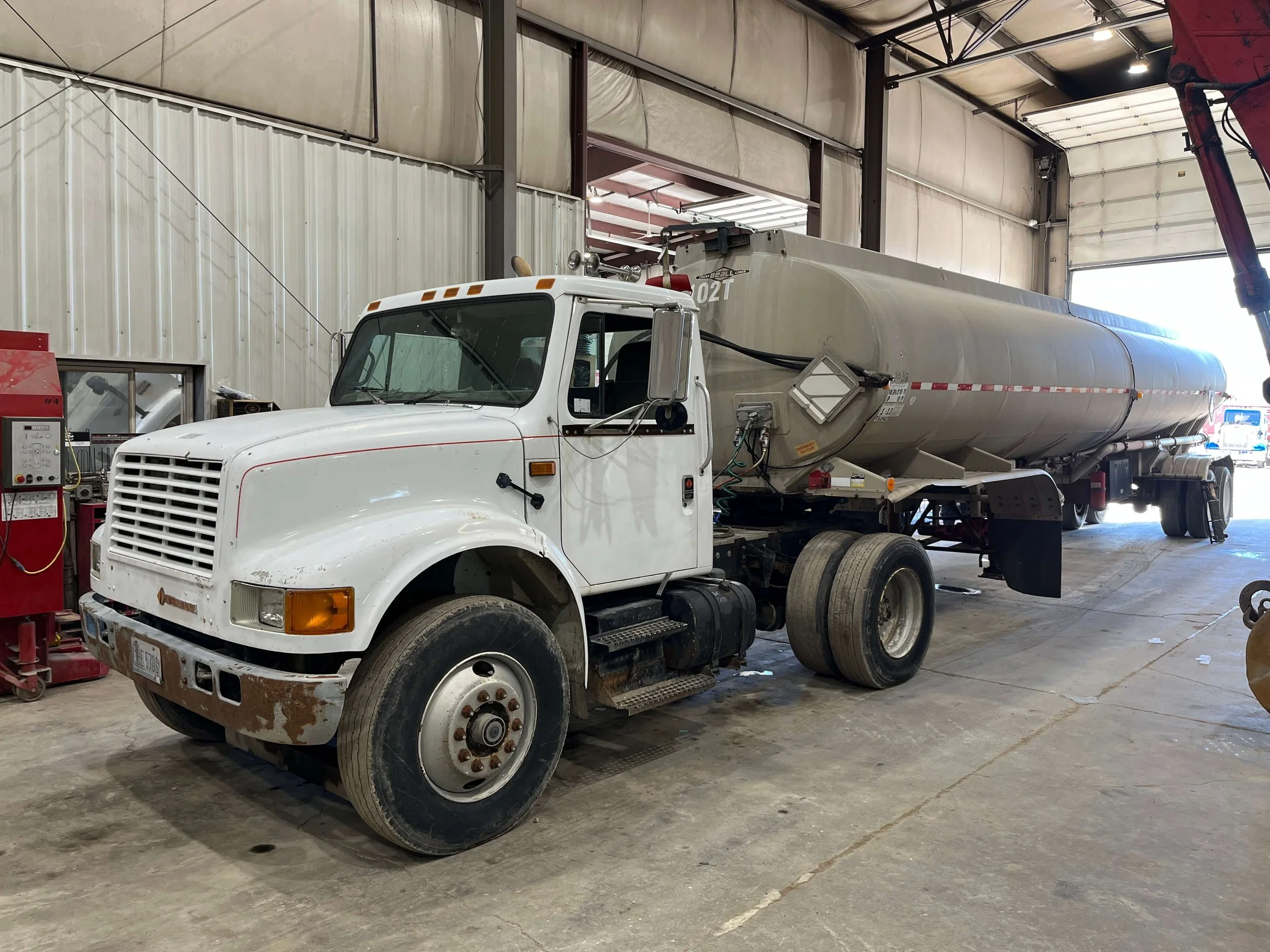 A white semi-truck with a large silver tanker trailer parked inside an industrial garage.