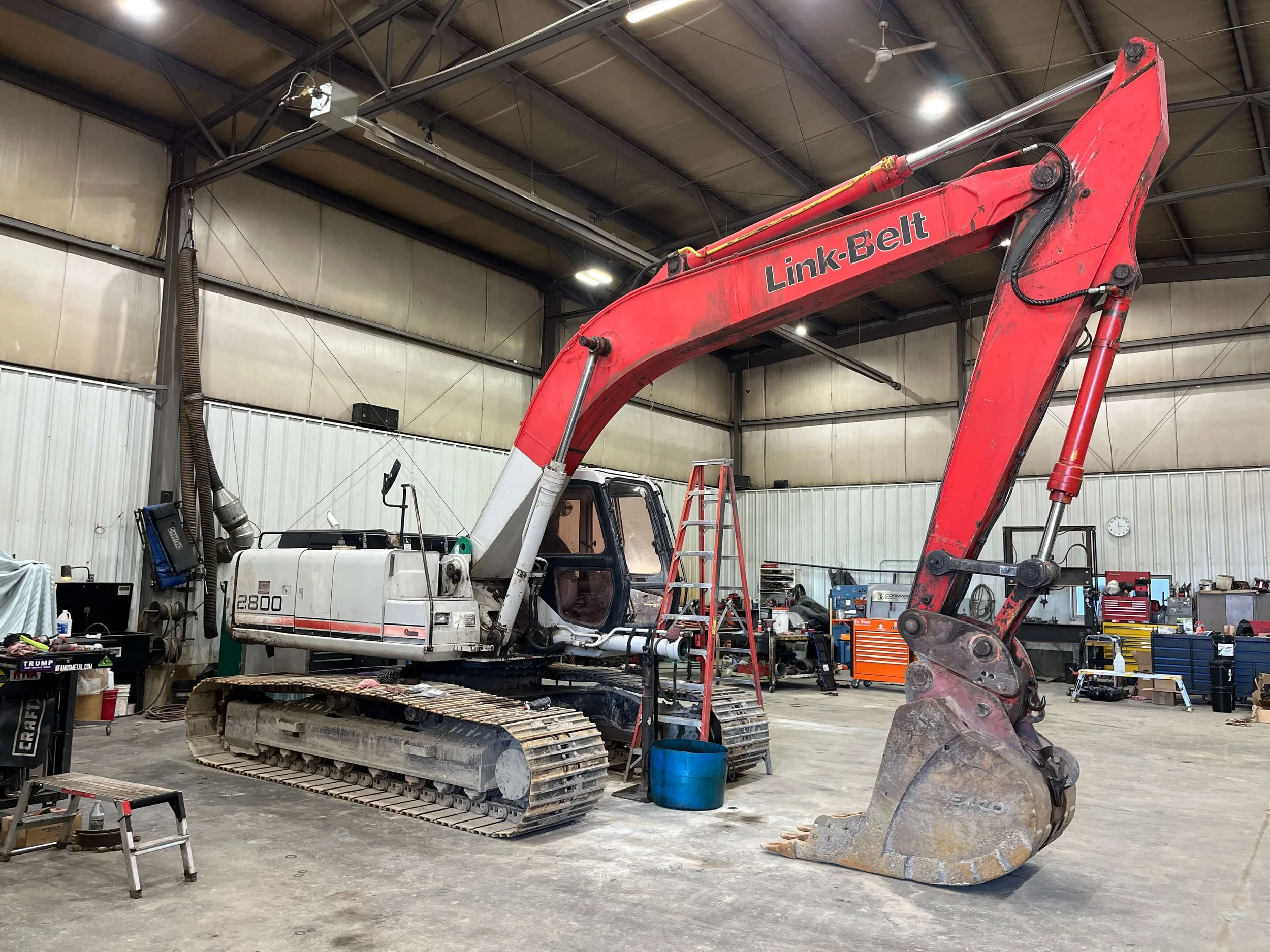 Large red and white excavator inside a spacious workshop with various tools and equipment.