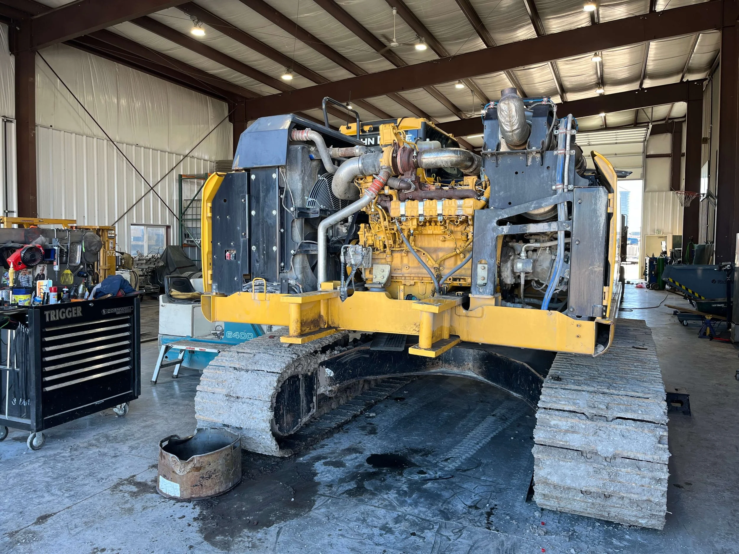 Construction vehicle being repaired in a workshop with exposed engine and tracked wheels.
