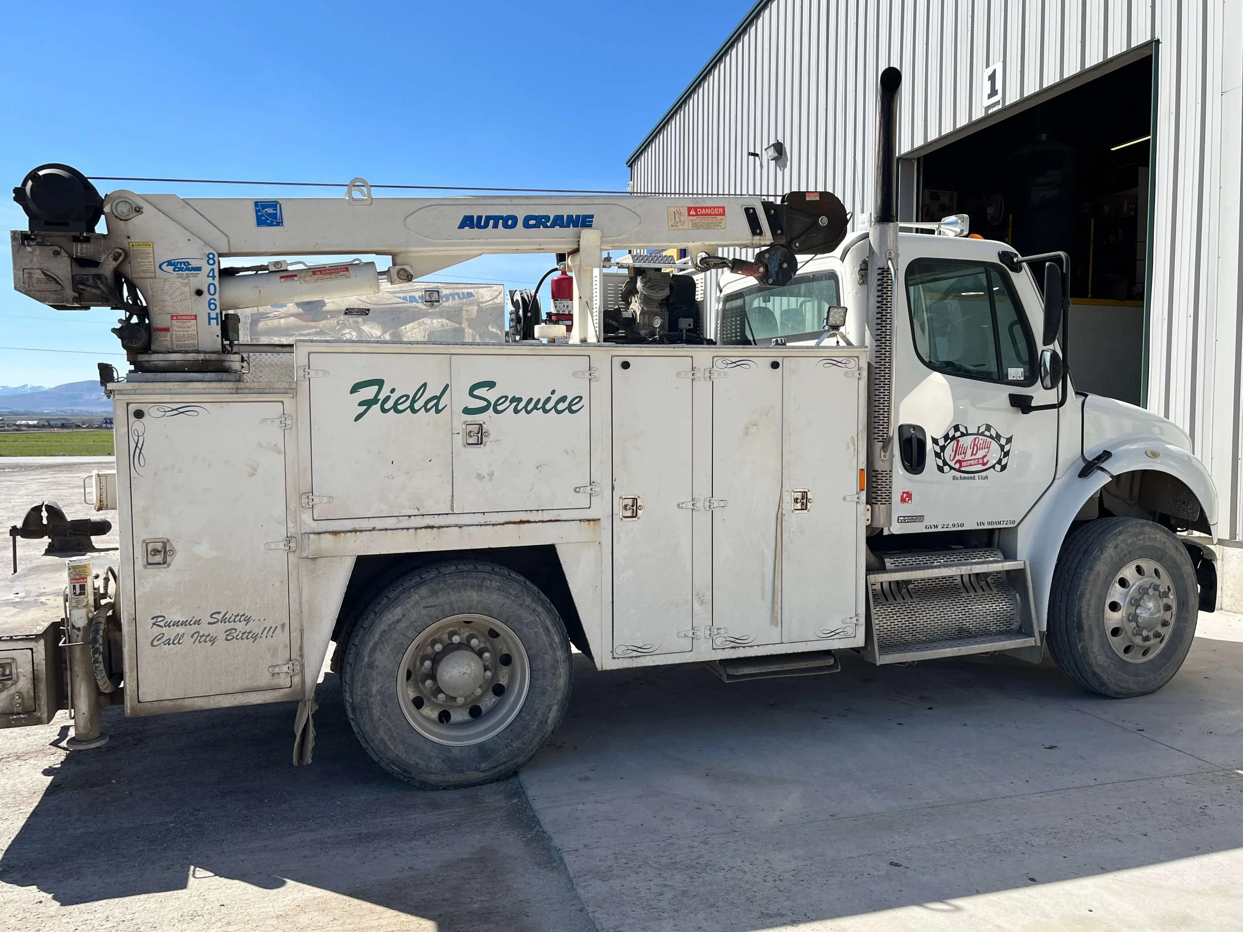Field service truck with crane parked outside a garage.