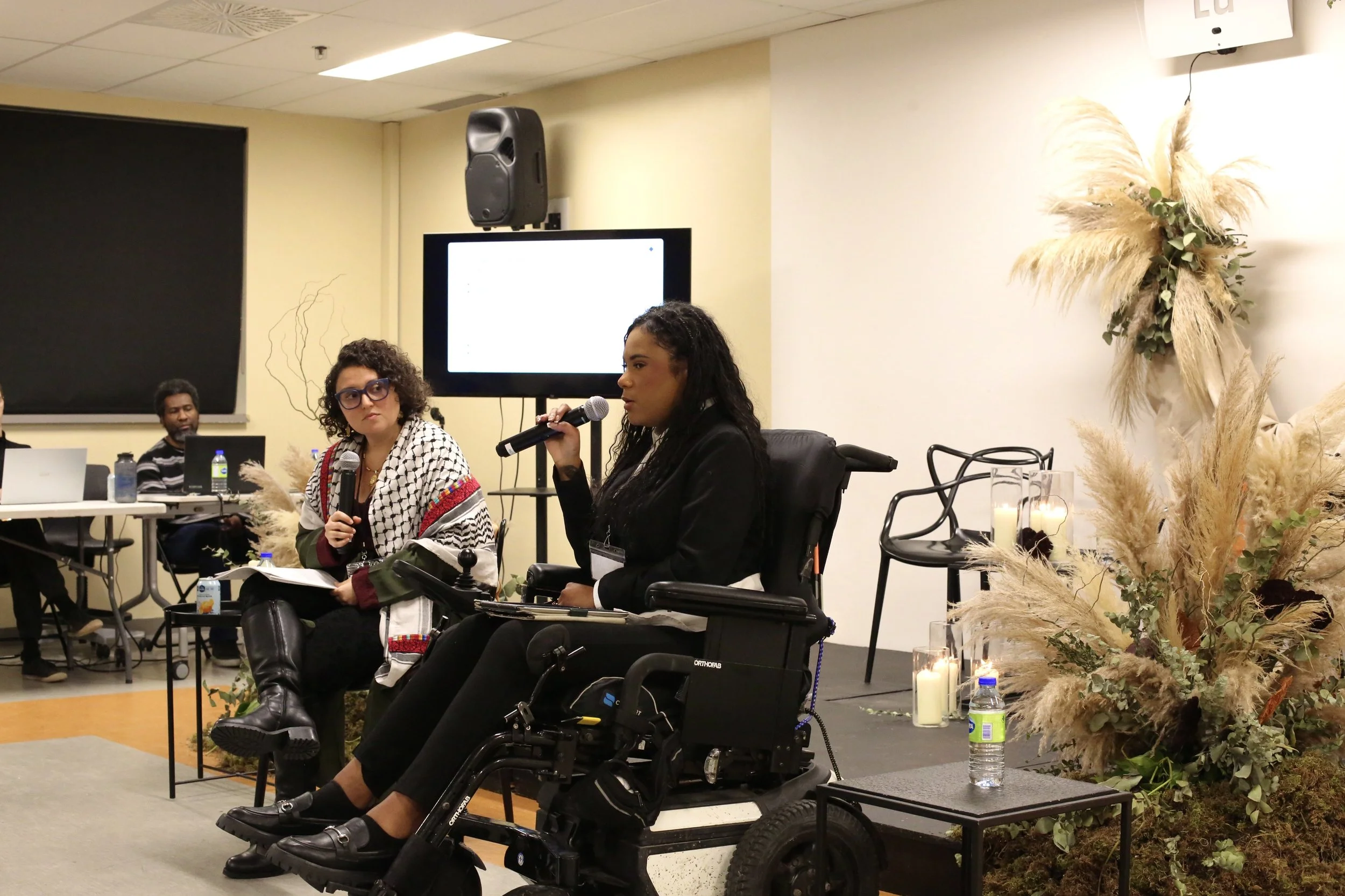 Allie at the “What if violence was perceived as a public health issue?” Symposium hosted by Éduconnexion. Allie is sitting in her motorized wheelchair next to disability justice and anti-racist feminist activist Nelly Bassily. Allie is wearing black 