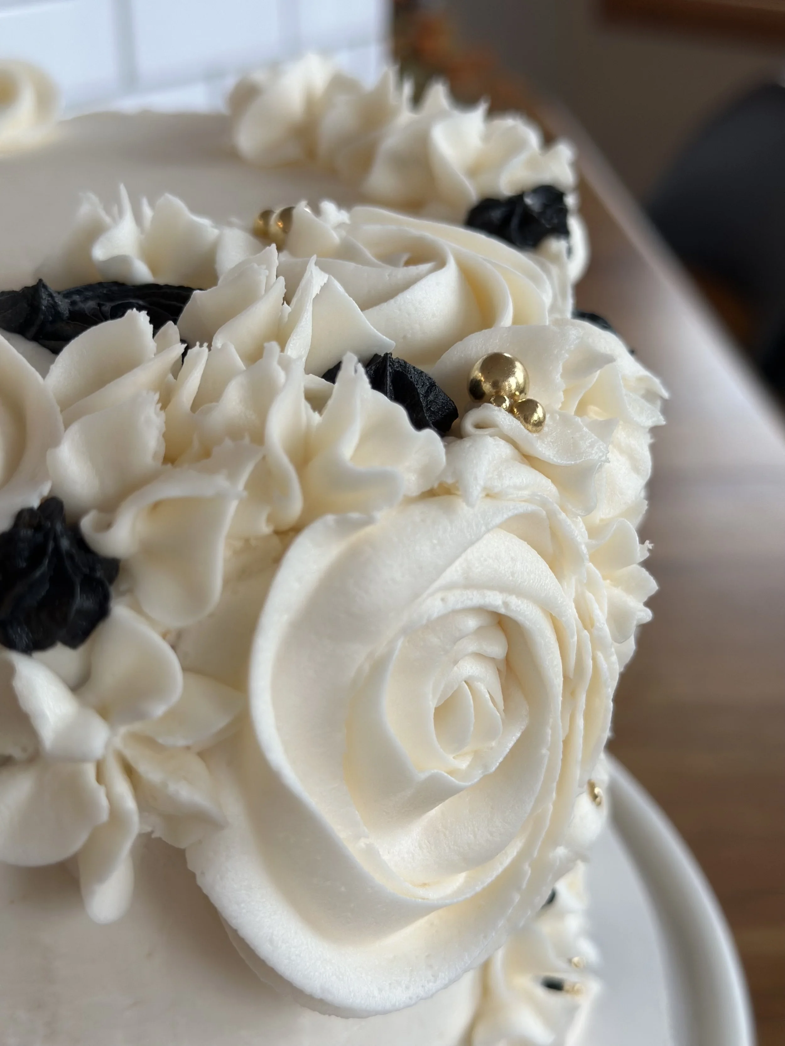 Close-up of a decorated white cake with piped white frosting, black decorative elements, and small golden beads.