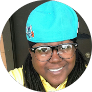 A woman with glasses wearing a bright blue cap, smiling.