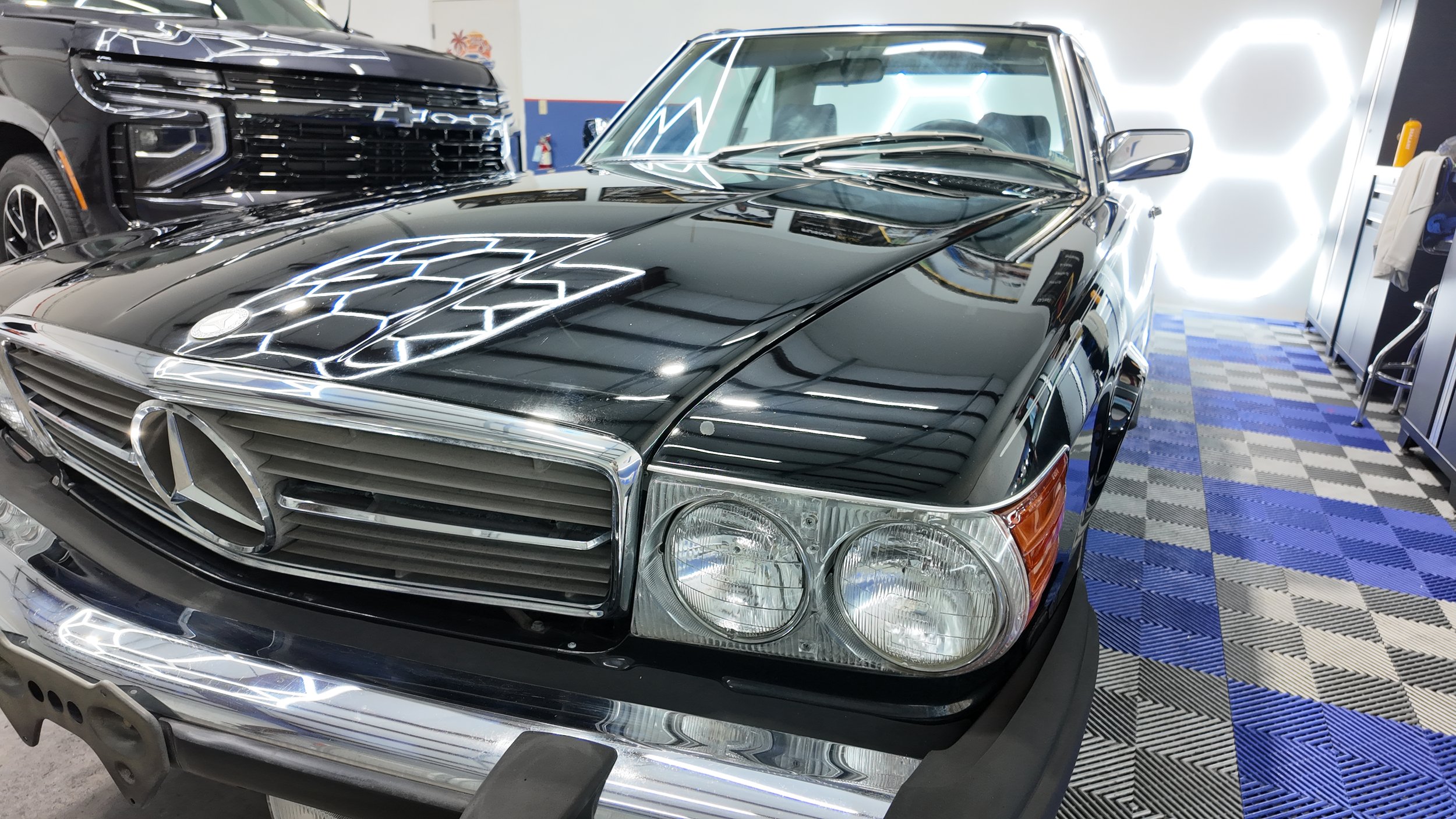 Black vintage Mercedes-Benz car parked indoors, reflecting ceiling lights on its polished surface.