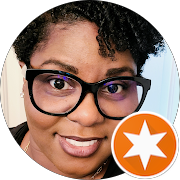 Close-up of a person with dark curly hair, glasses, and a friendly expression cutting off at the shoulders.