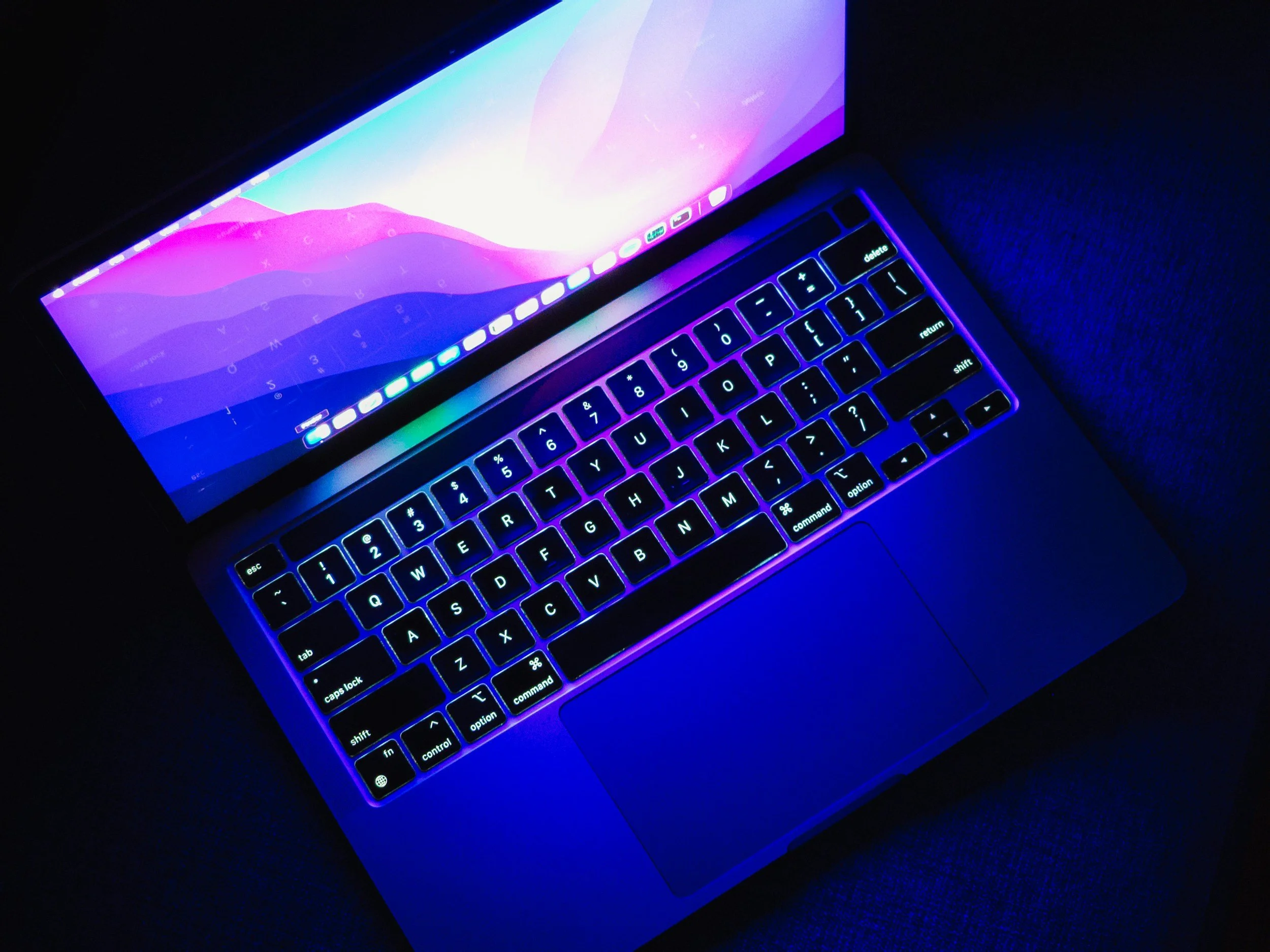 A laptop with backlit keys and a colorful display screen showing a wave pattern in purple, pink, and blue colors.