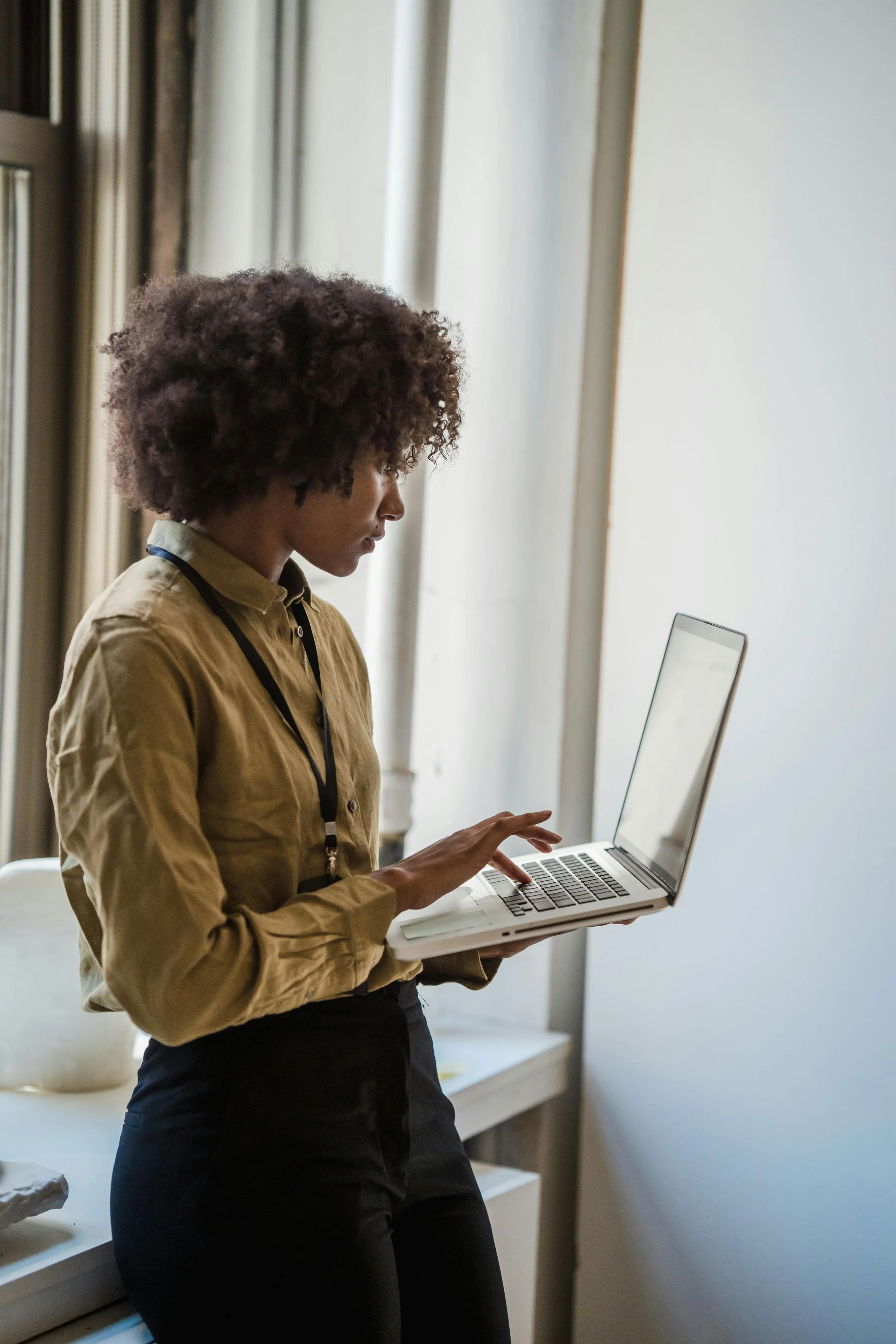 A woman with curly hair using a laptop in a room with white walls and curtains.