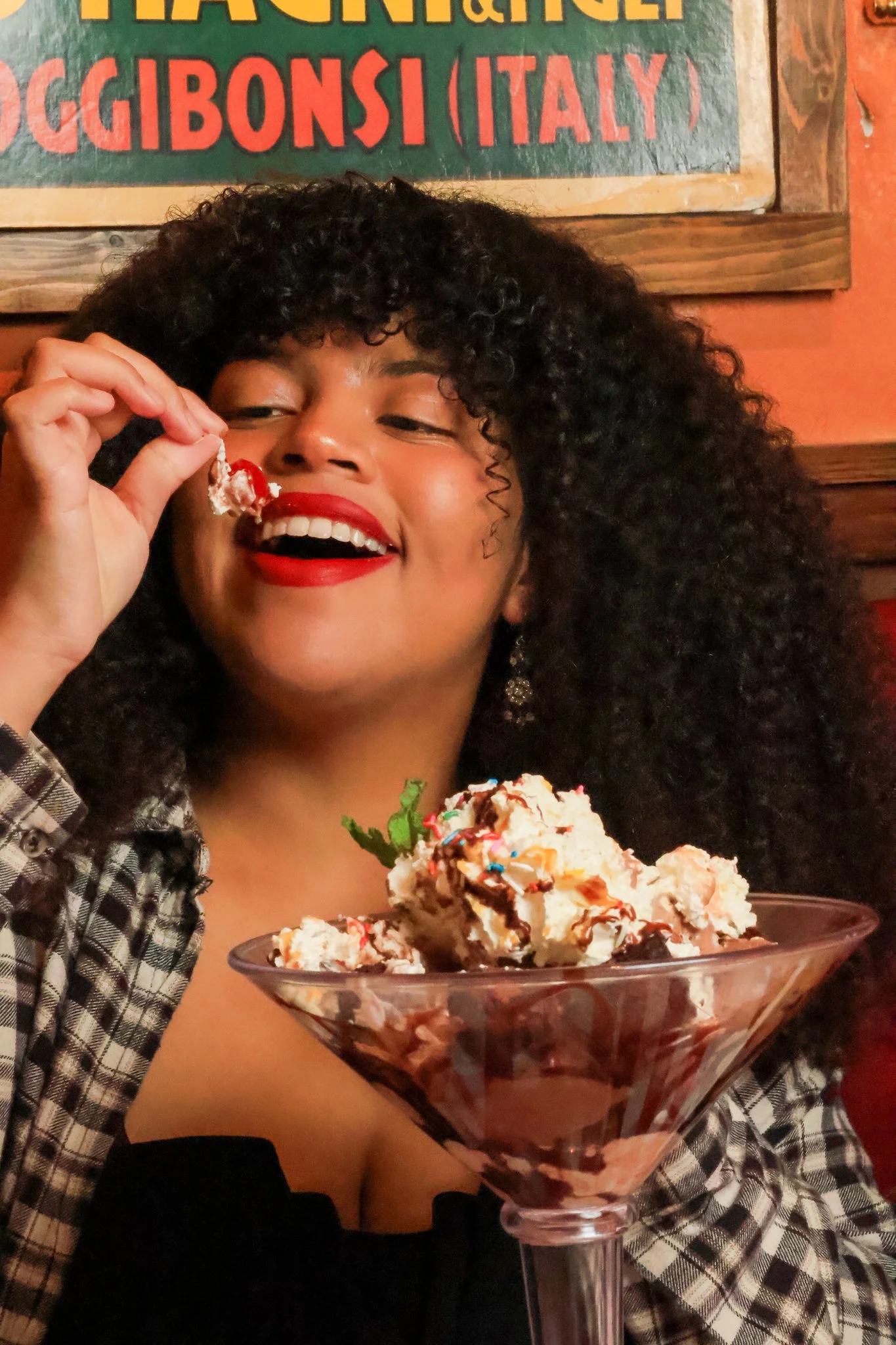 Woman with curly hair and red lipstick enjoying ice cream in a restaurant