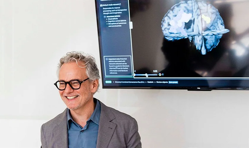 Dr. Reitano smiling in front of a screen displaying information for TMS for PTSD near Charleston Heights, Las Vegas, NV.
