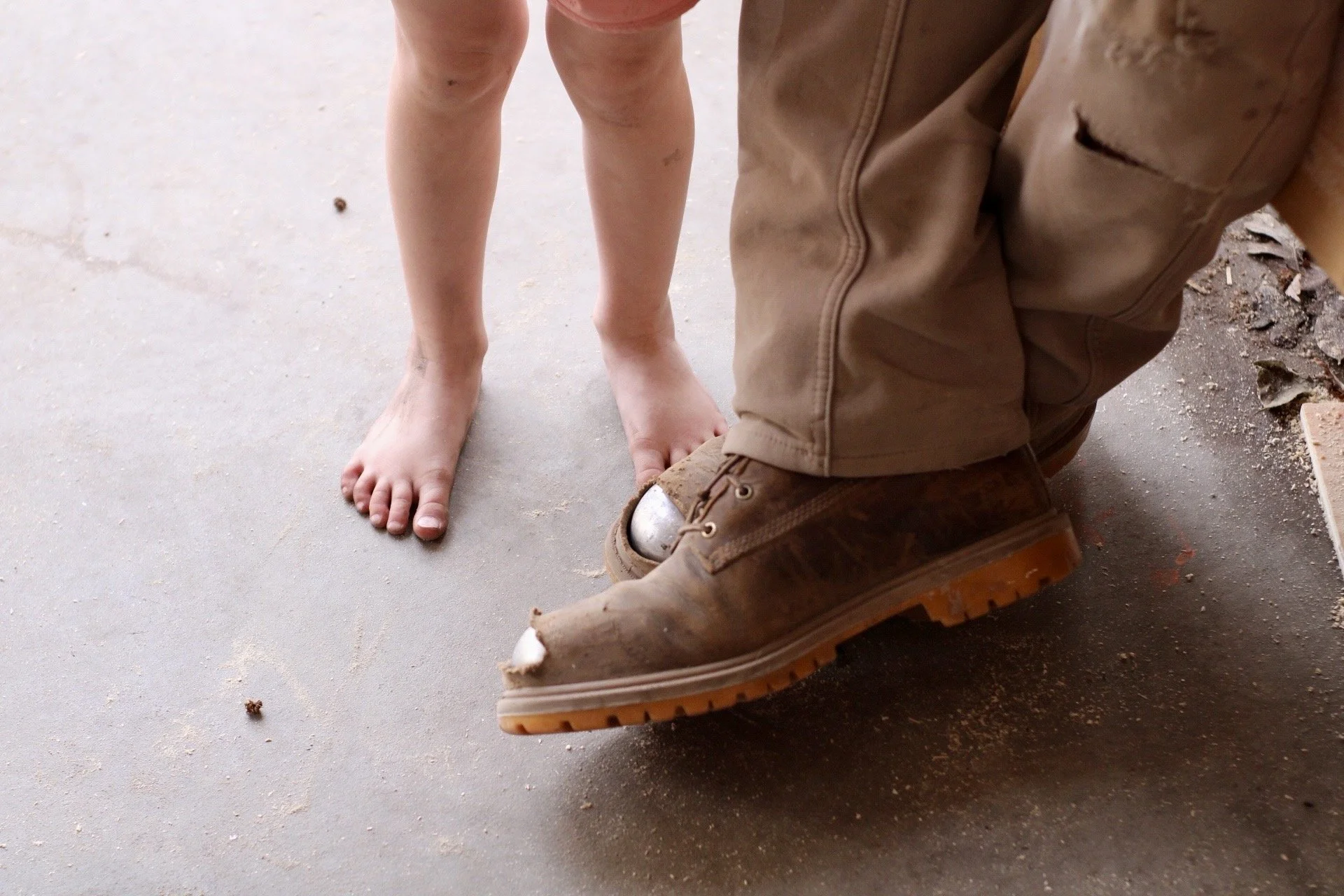 Working boots next to child's bare feet