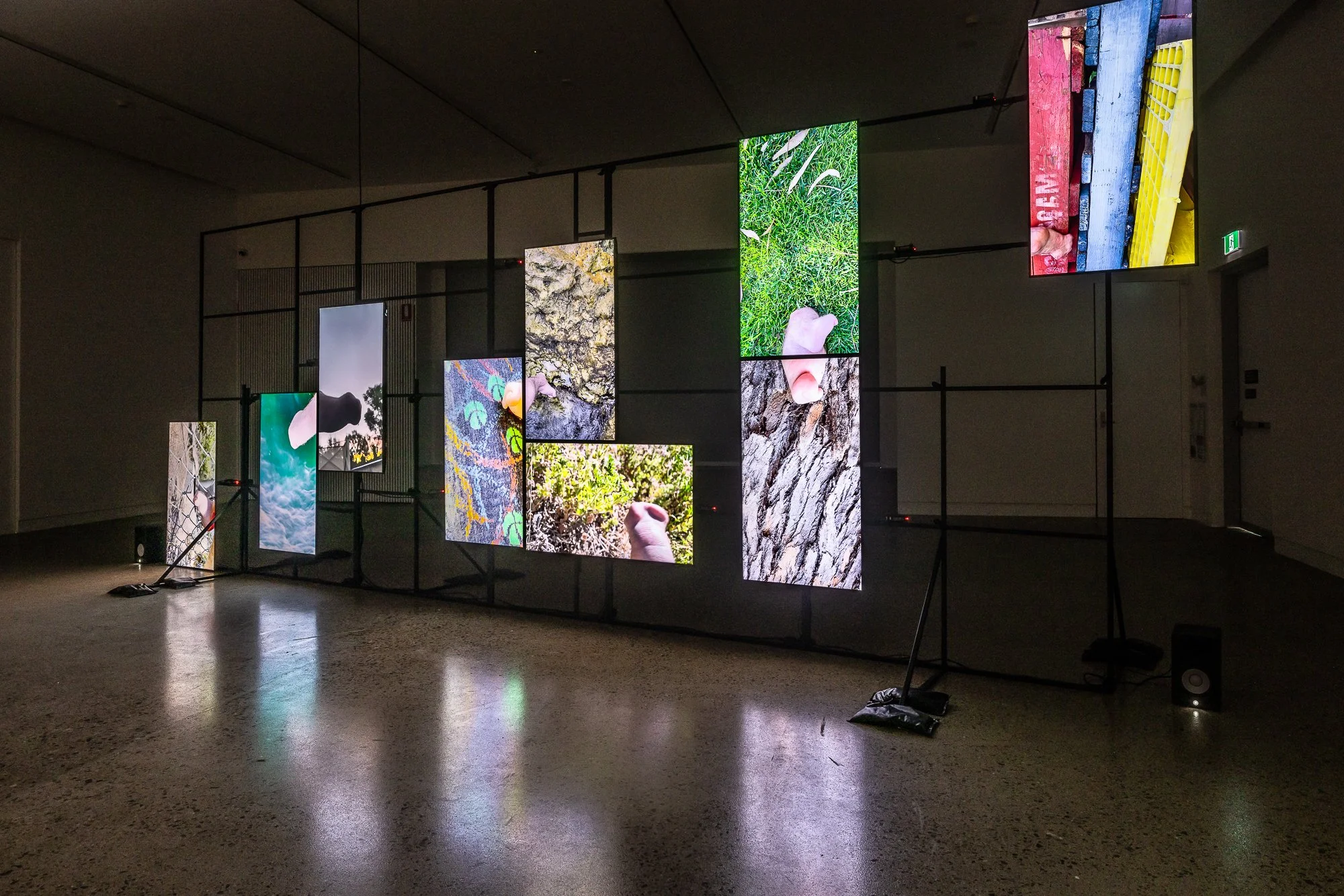 Indoor art installation with multiple LED screens displaying various colorful images, mounted on a black metal framework in a dark room.