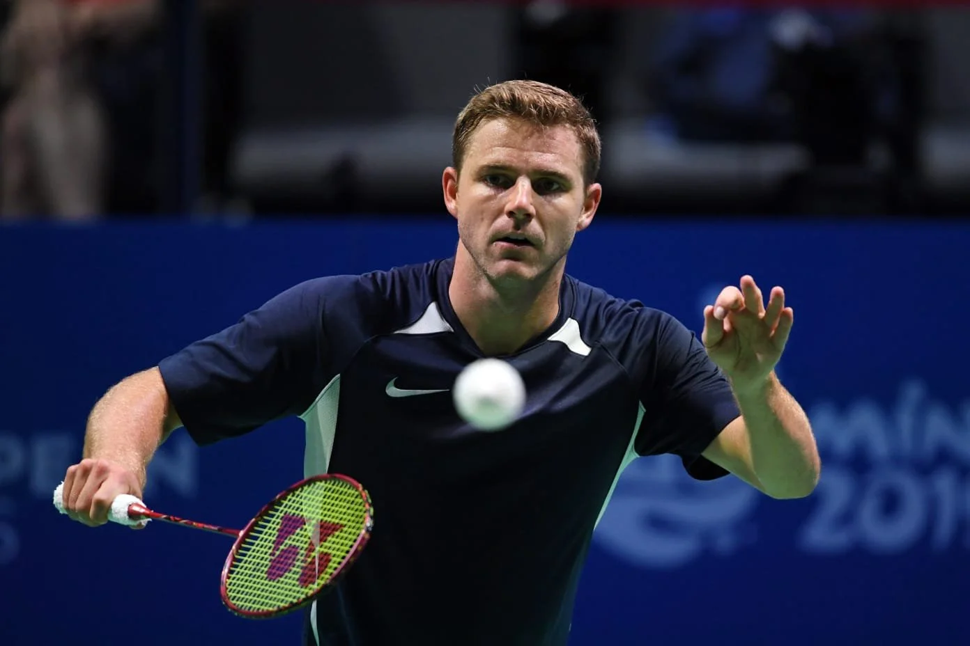Badminton player hitting shuttlecock in action on court with blurred background.