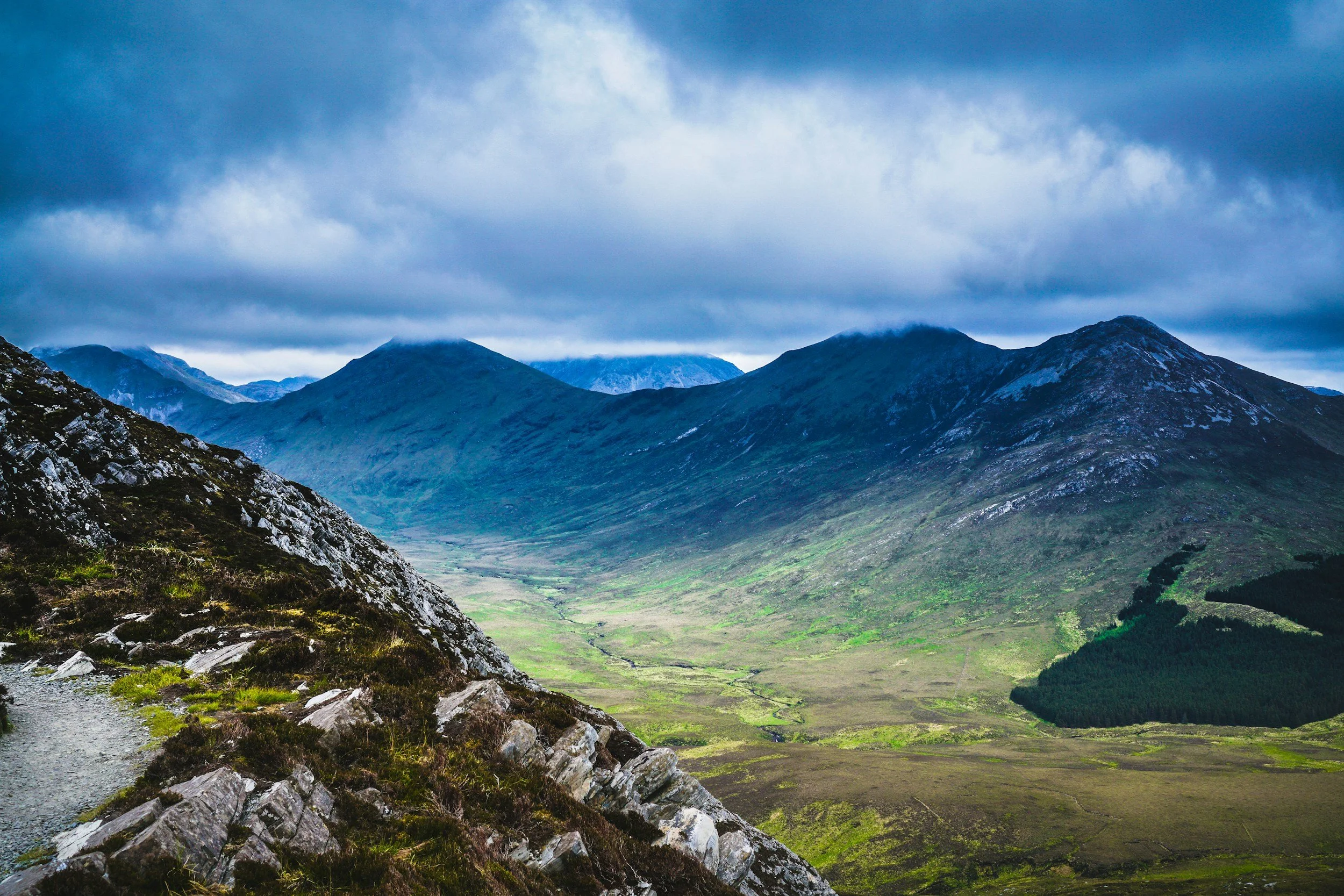 Scenic view of a valley surrounded by tall mountains with a cloudy sky overhead.