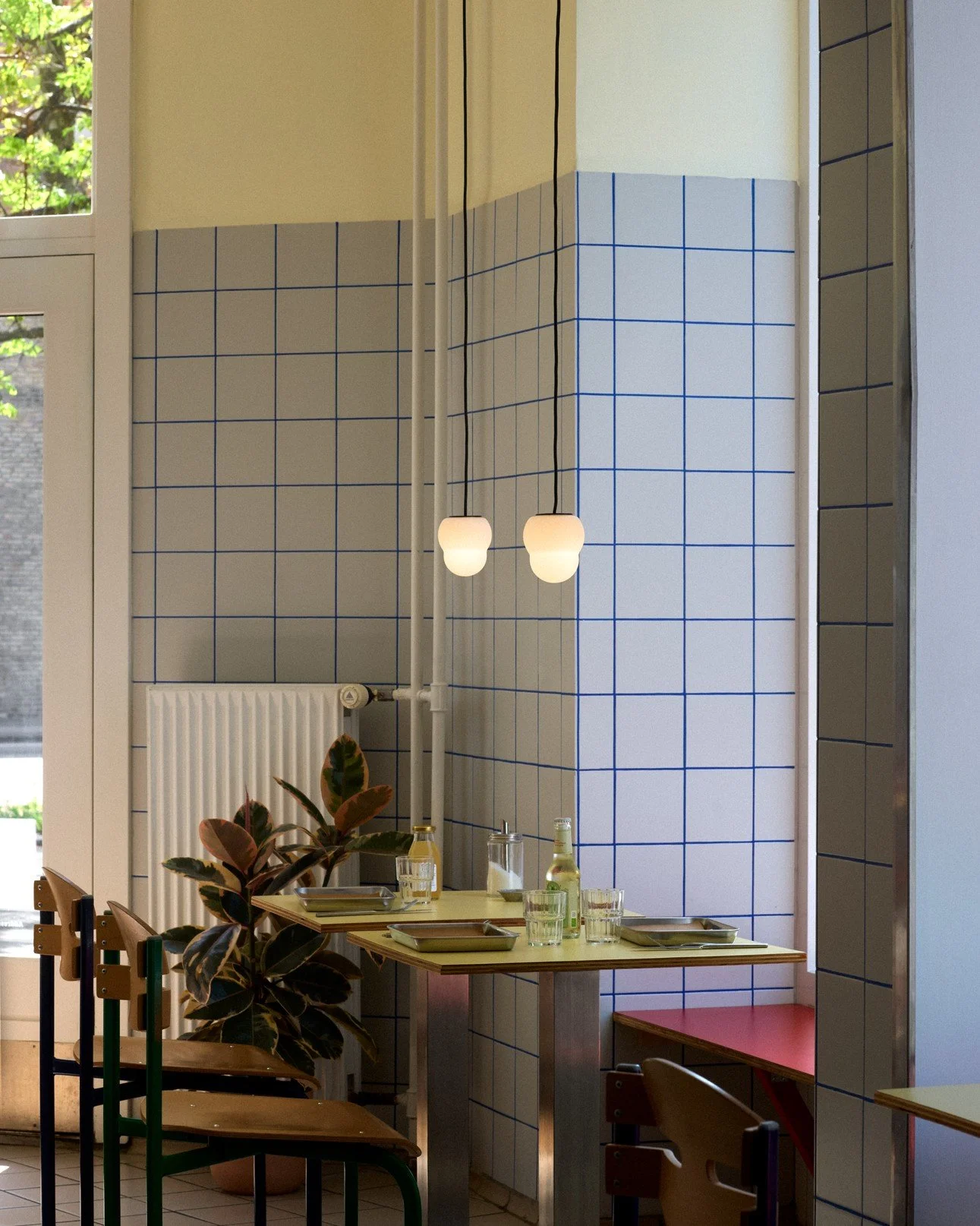 Interior of a modern restaurant with a table set with glasses and bottles, featuring a wall with blue grid-tile pattern and two hanging pendant lights.