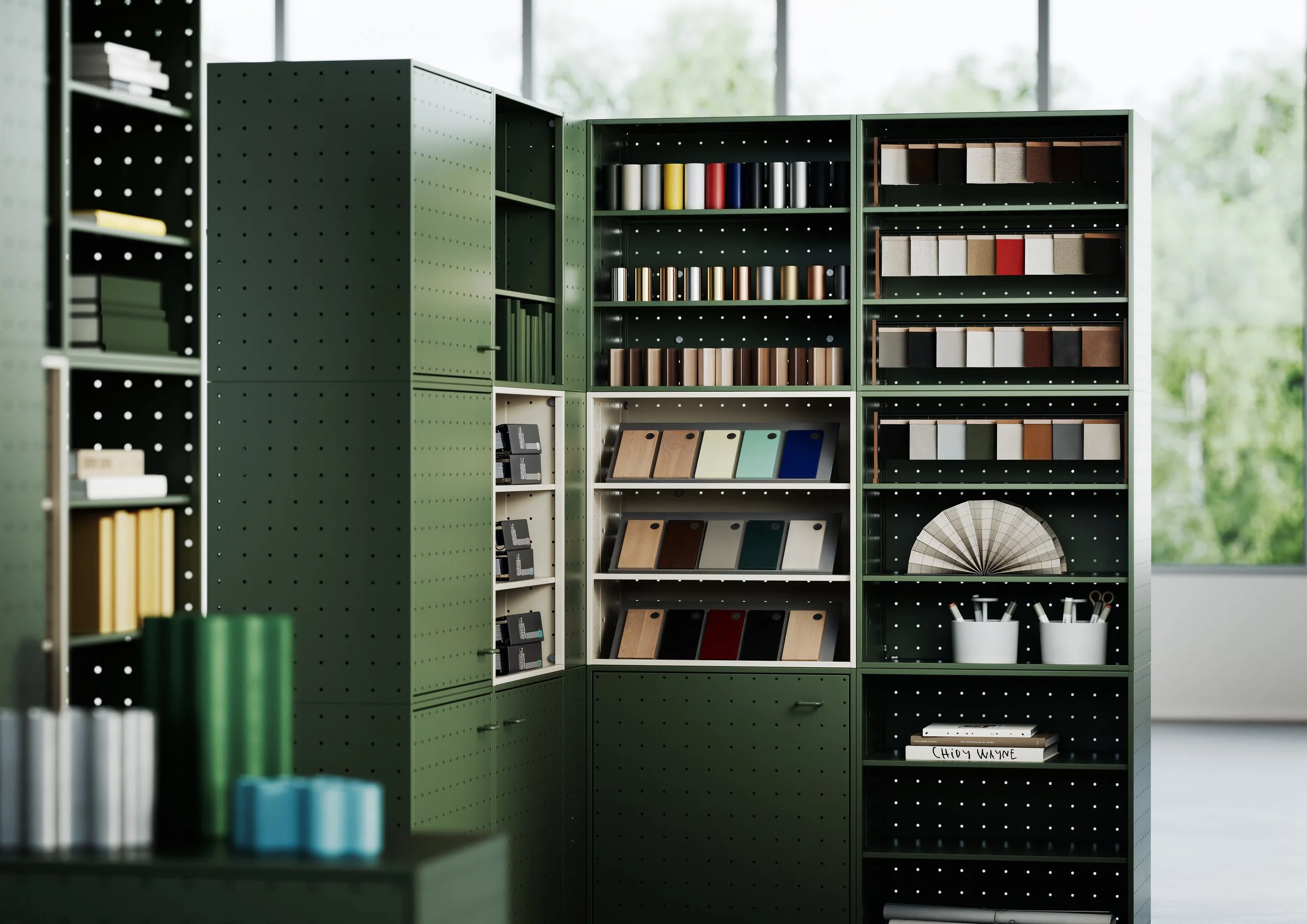 Green shelving units with fabric swatches, color samples, and design materials in a modern office or showroom setting.