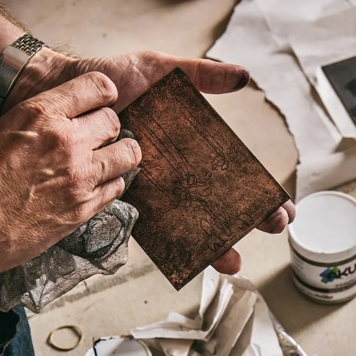 close up shot of artist rubbing ink onto a copper printing plate with dirty rag