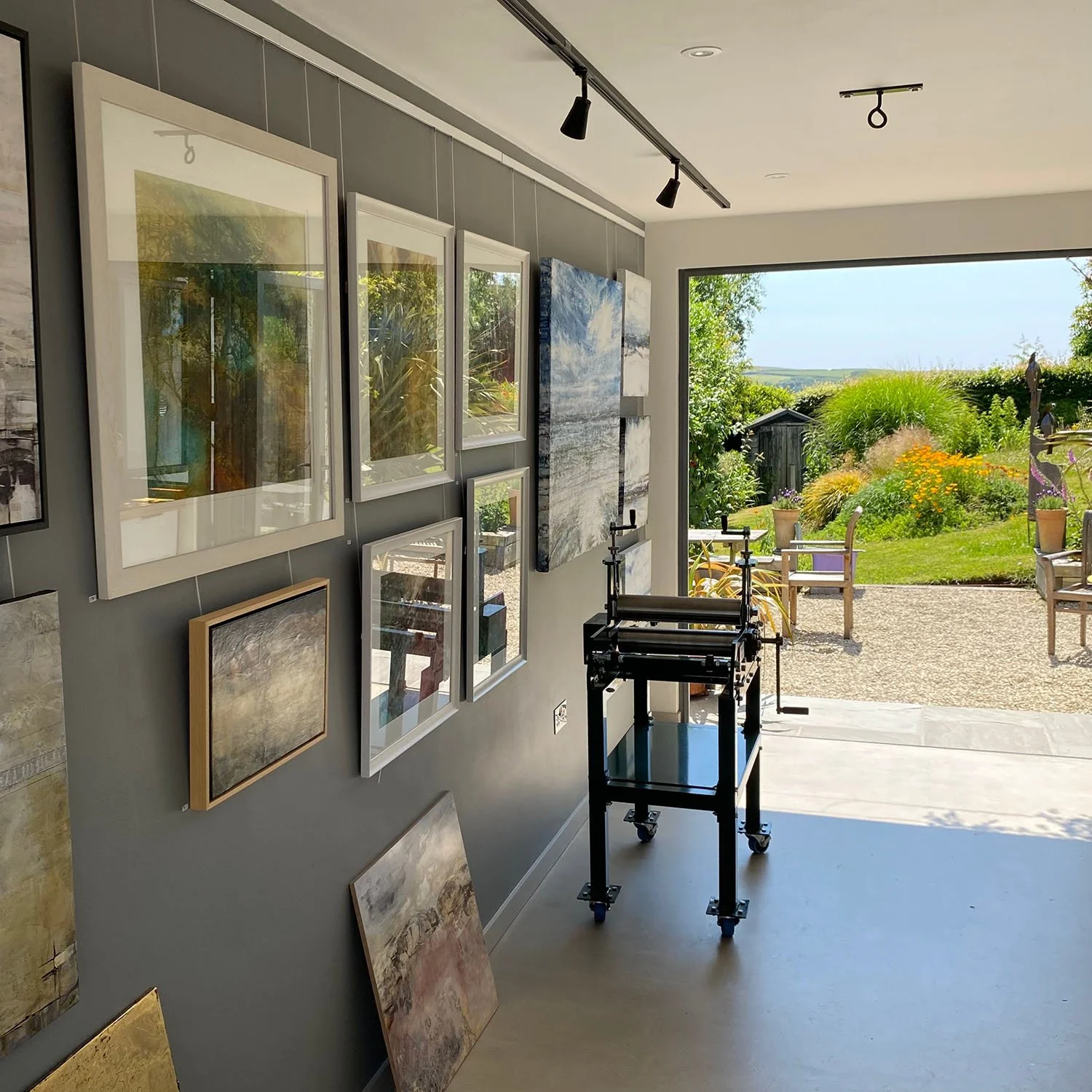 Interior shot of art gallery with doors opening onto garden and printing press in foreground