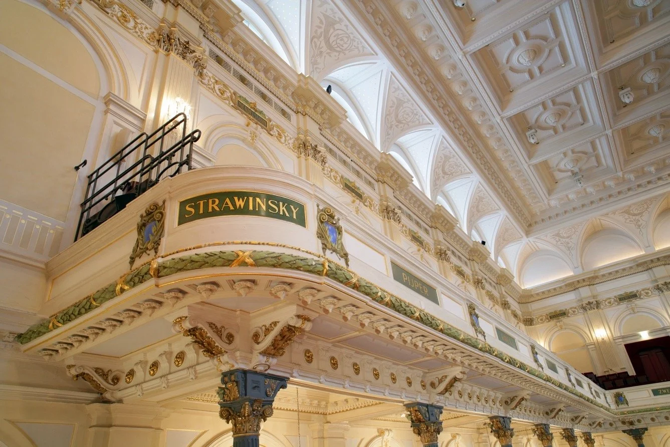 Interior of a Het Concertgebouw hall in Amsterdam with ornate architectural details, include decorative columns and balconies, and a prominent sign reading 'Strawinsky', the famous composer.