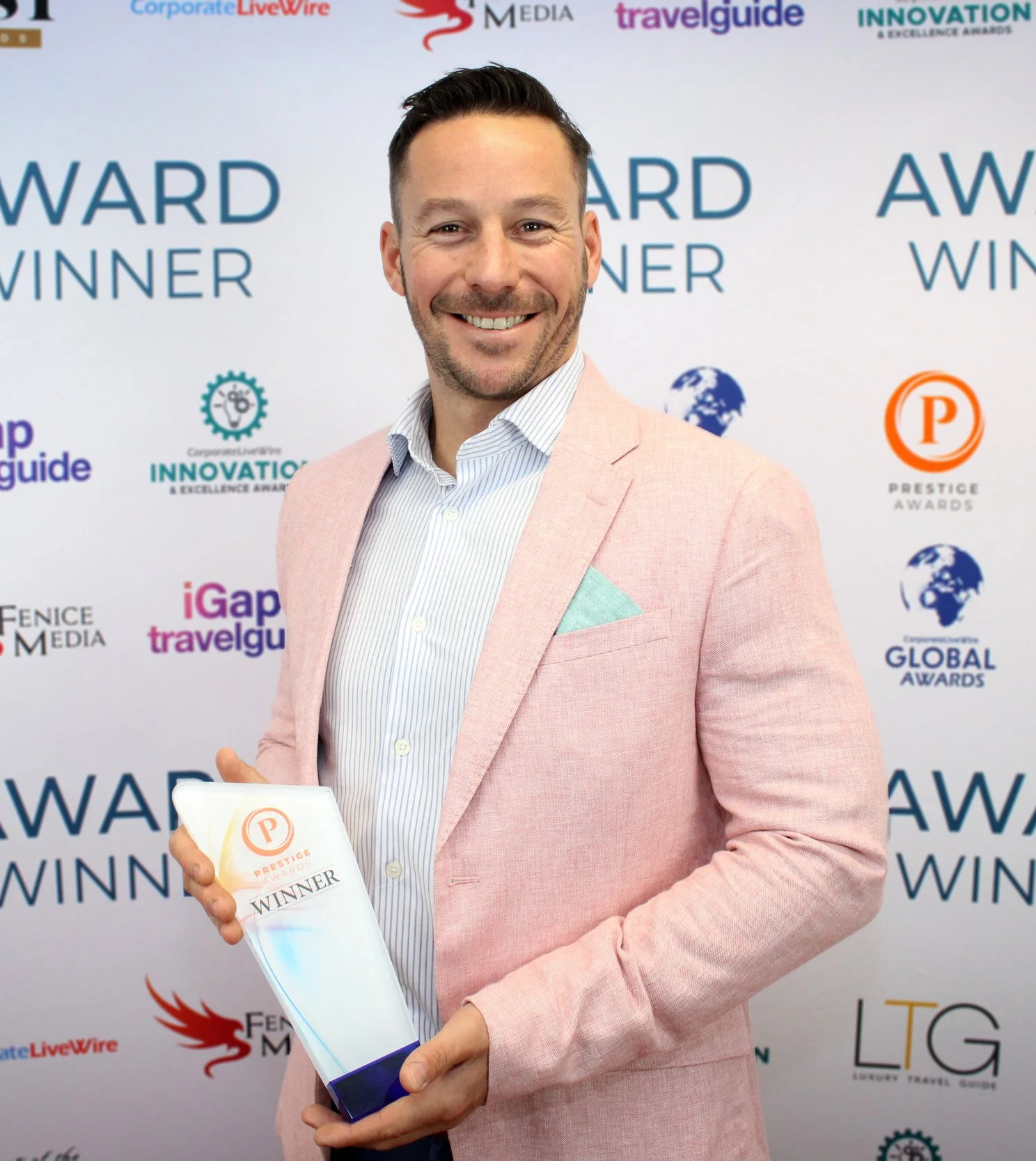 A man in a pink blazer holding an award trophy at an awards event.