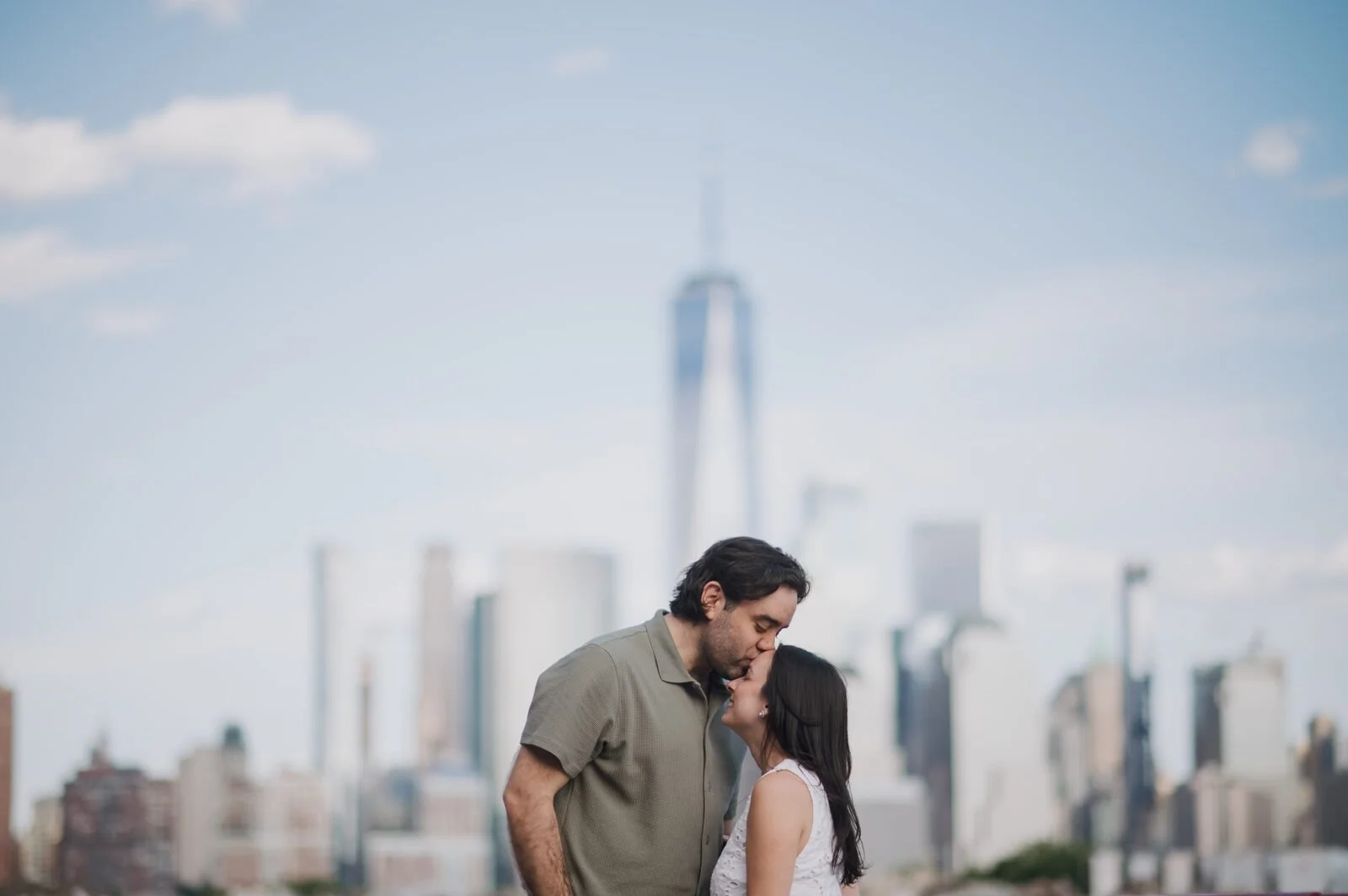 Engaged couple sharing their first NYC engagement kiss with One World Trade Center and the Manhattan skyline behind them