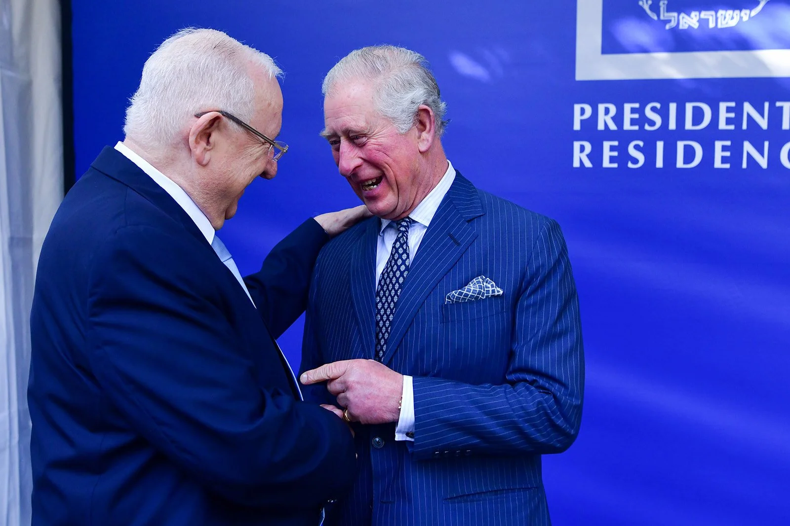 King of England and the president of Israel in a friendly conversation, with one of them touching the other's shoulder.