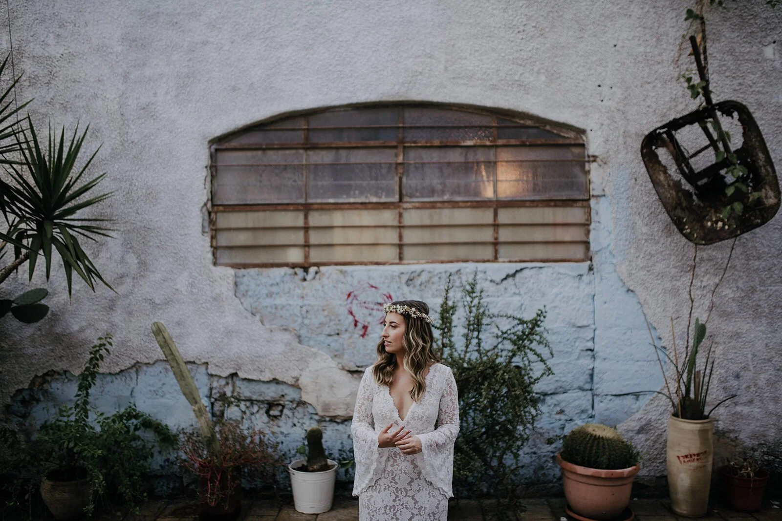 Bride in a lace boho gown wearing a floral crown, standing against a sun-bleached wall