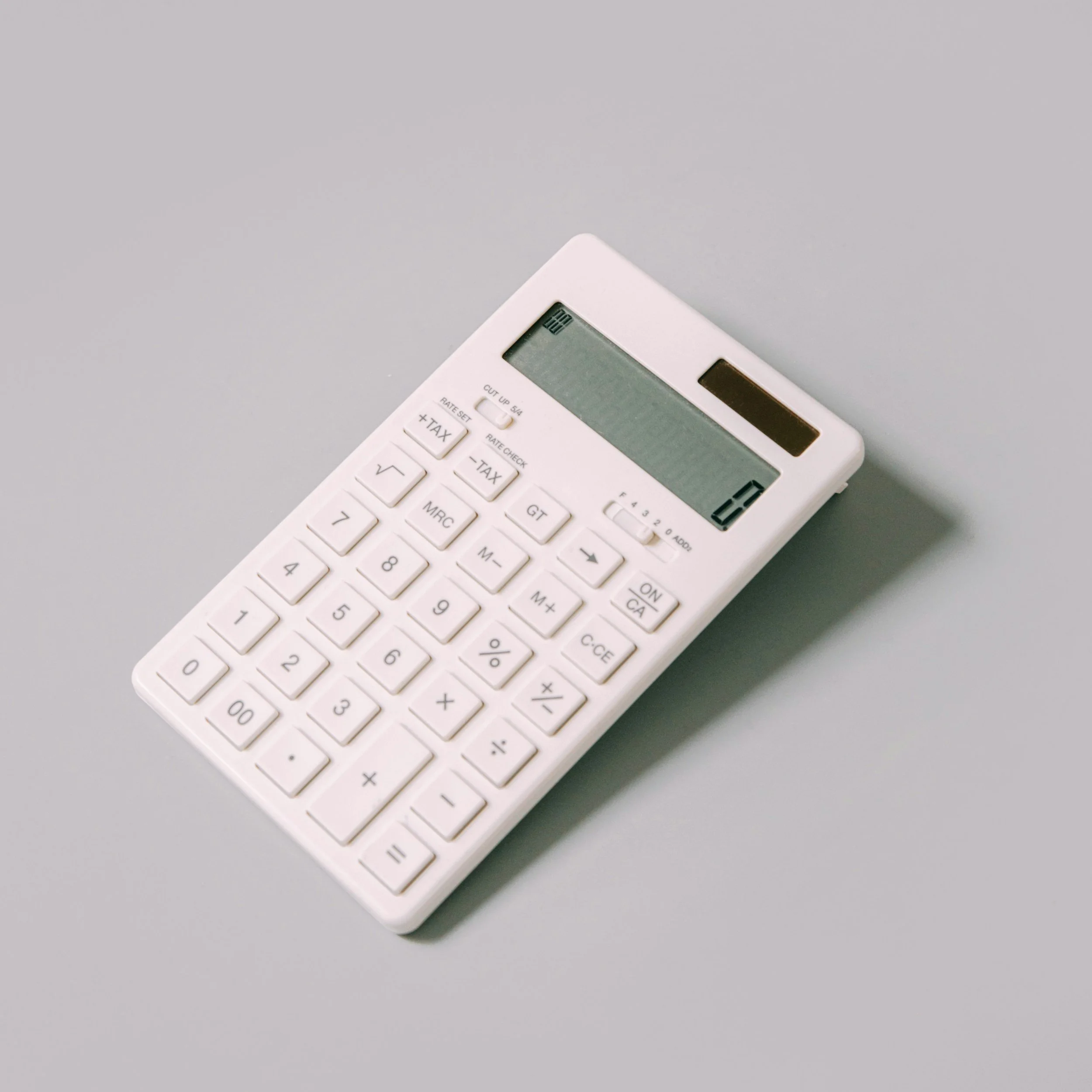 Une calculatrice blanche posée sur une surface gris clair, vue partielle.
