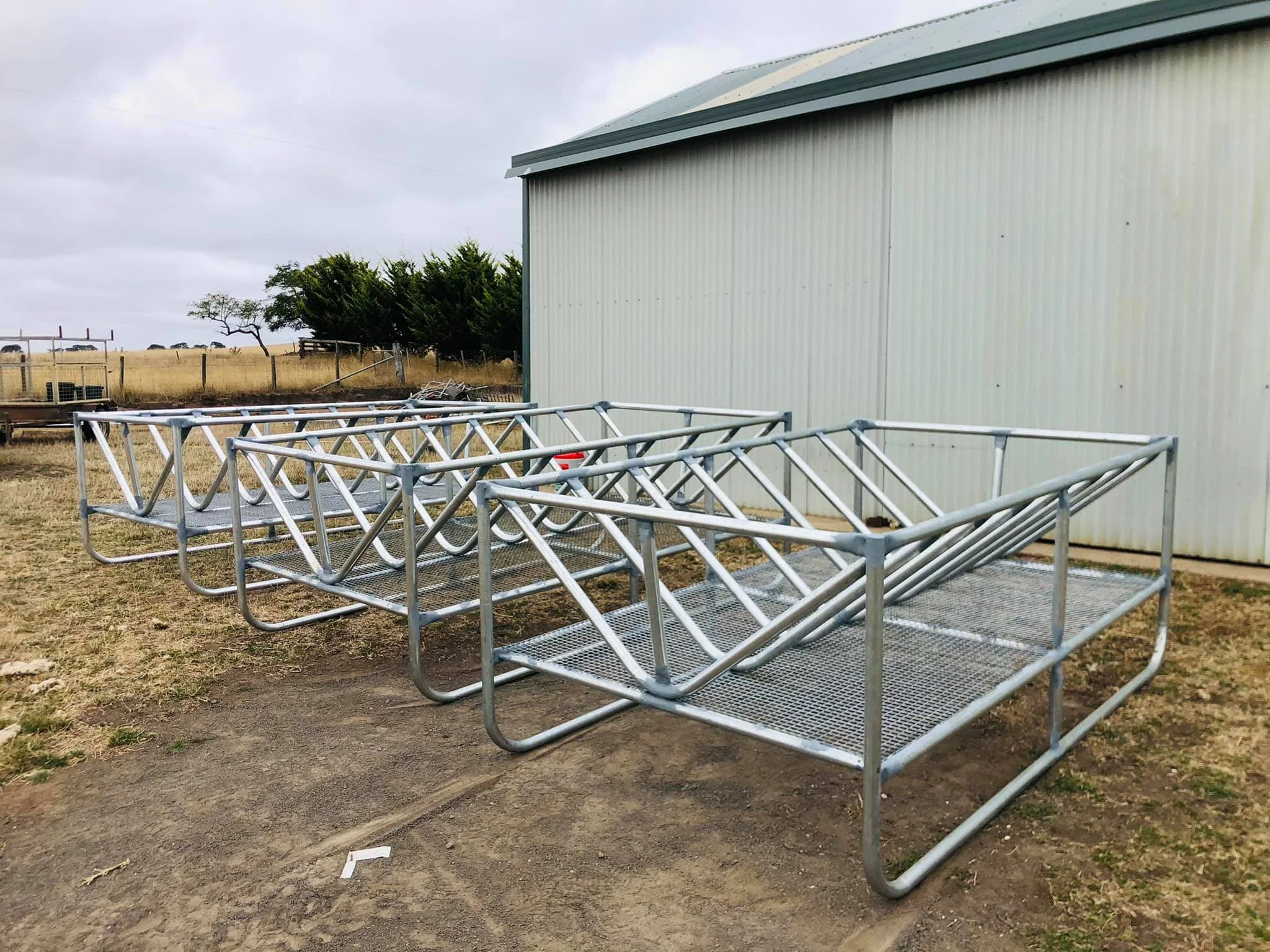Metal bleacher seating with a large white building and a farm landscape in the background, under a cloudy sky.