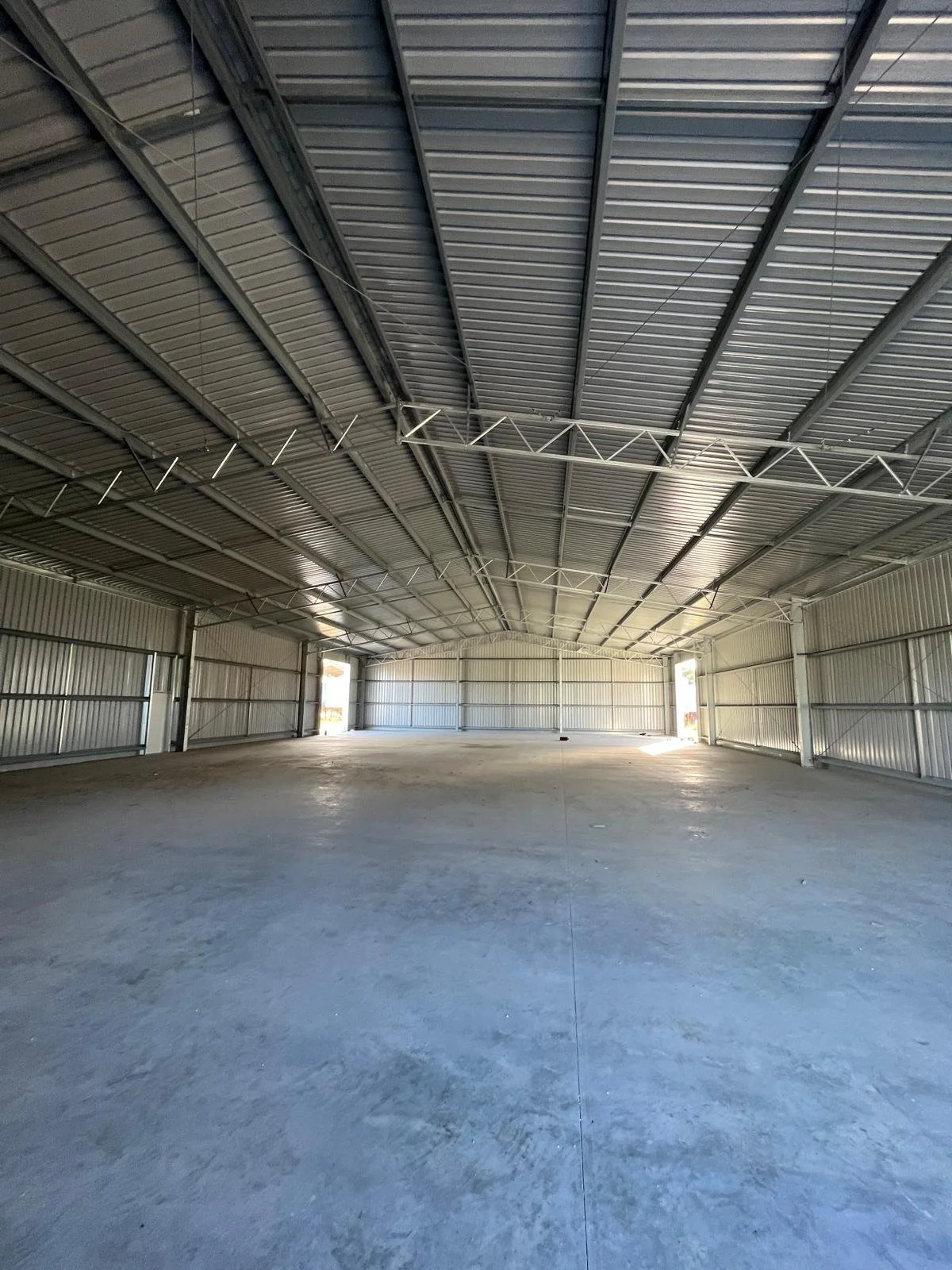 Empty industrial warehouse with metal walls and ceiling, concrete floor, and open large garage doors at the back.