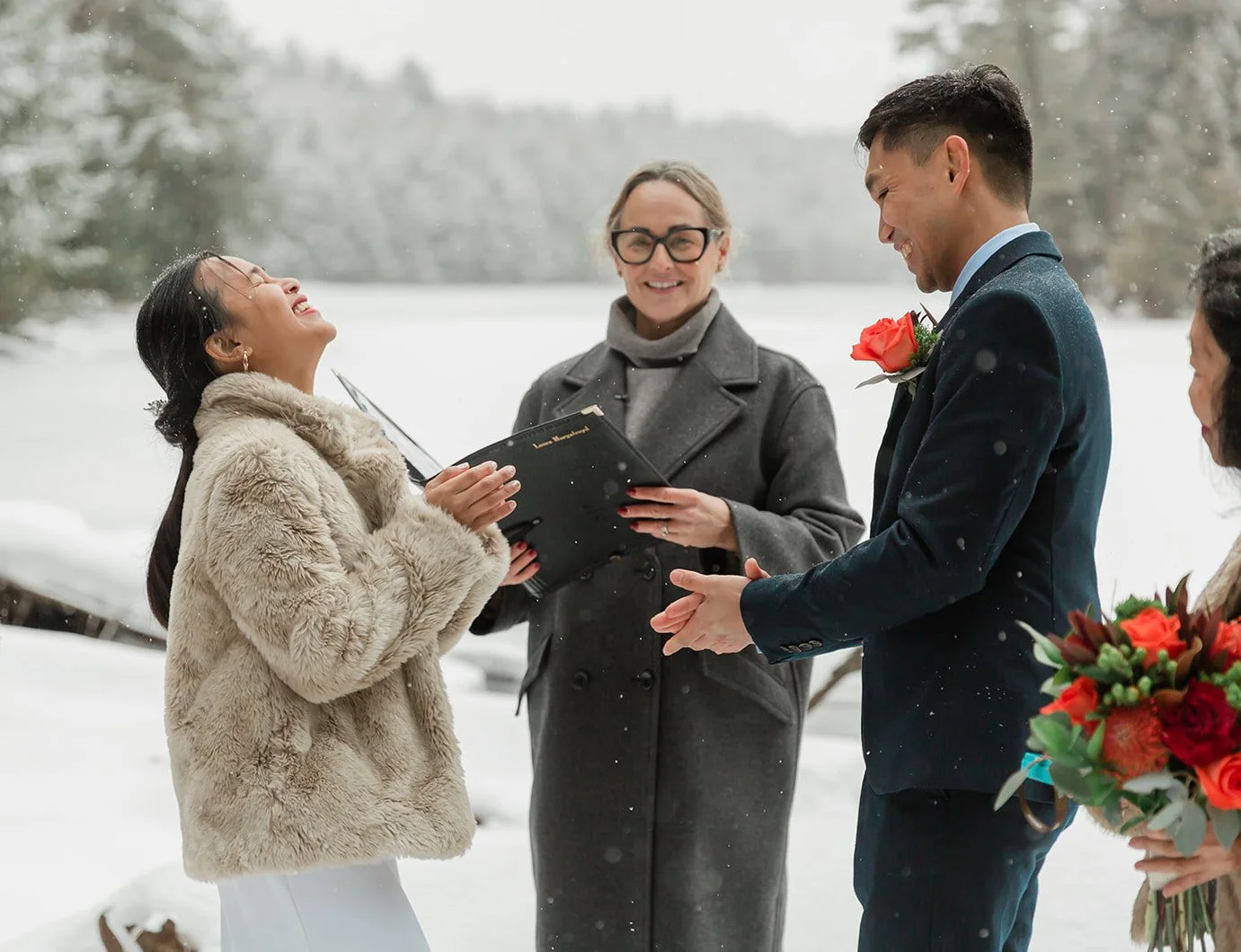 A couple gets married outdoor in the snow, exchanging vows with an officiant and an officiant holding a bouquet of red and orange flowers.