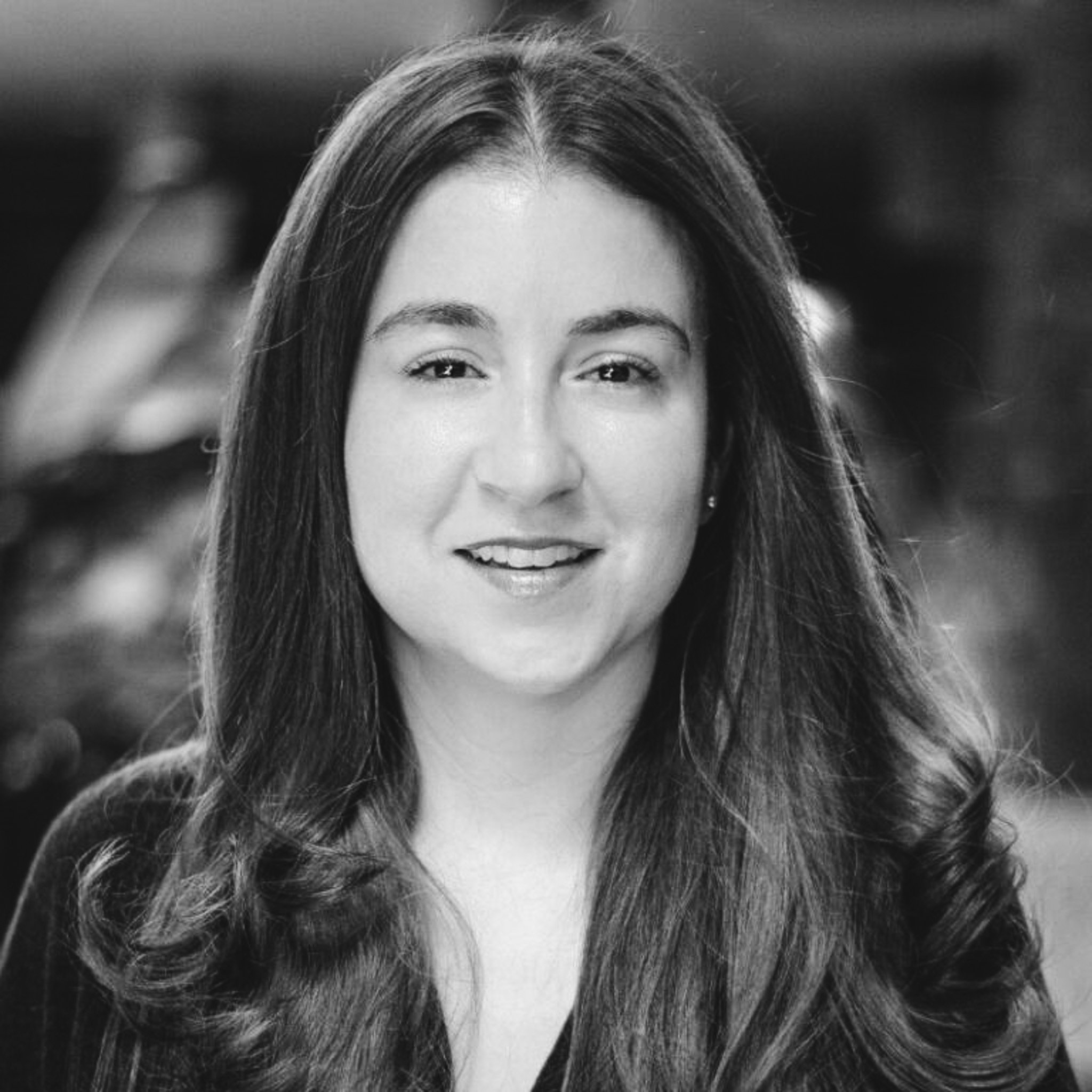 A black and white portrait of a smiling woman with long, wavy hair. She is looking directly at the camera and appears to be in a well-lit indoor setting.