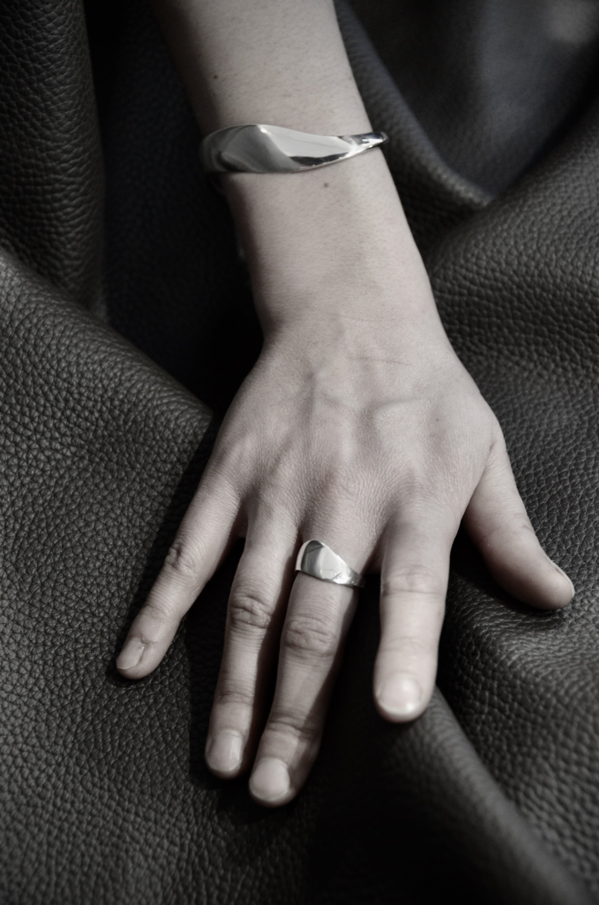 Une main portant une bague et un bracelet en argent Jacques Moniquet, posée sur un tissu noir.