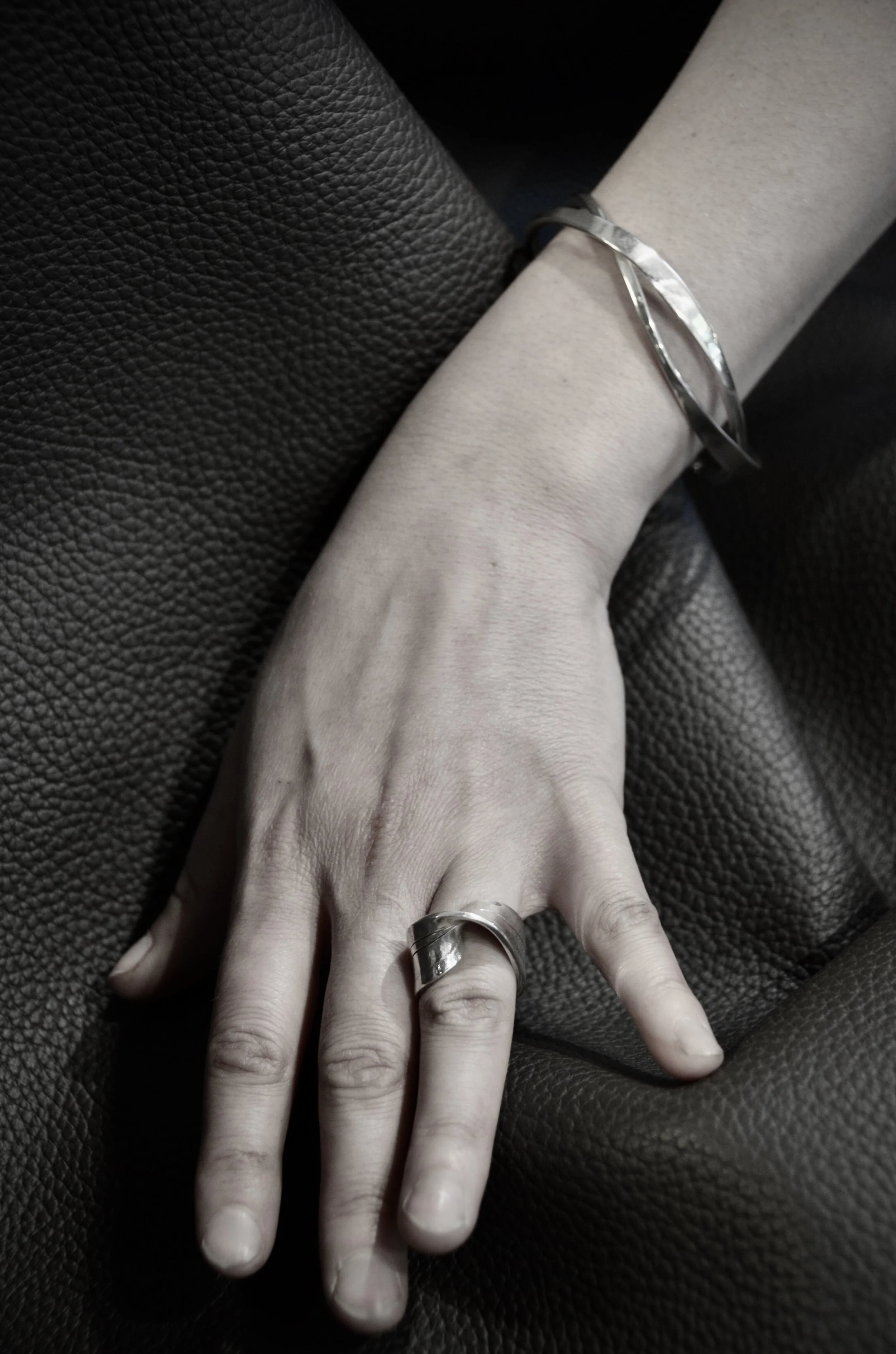 Une main portant une bague et un bracelet en argent Jacques Moniquet, posée sur un tissu noir.