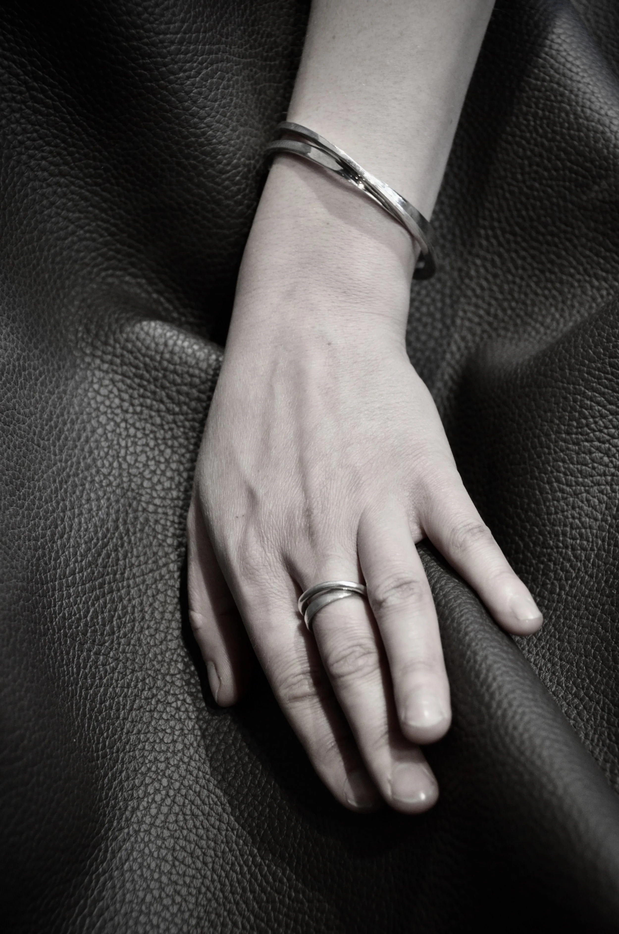 Une main portant une bague et un bracelet en argent Jacques Moniquet, posée sur un tissu noir.