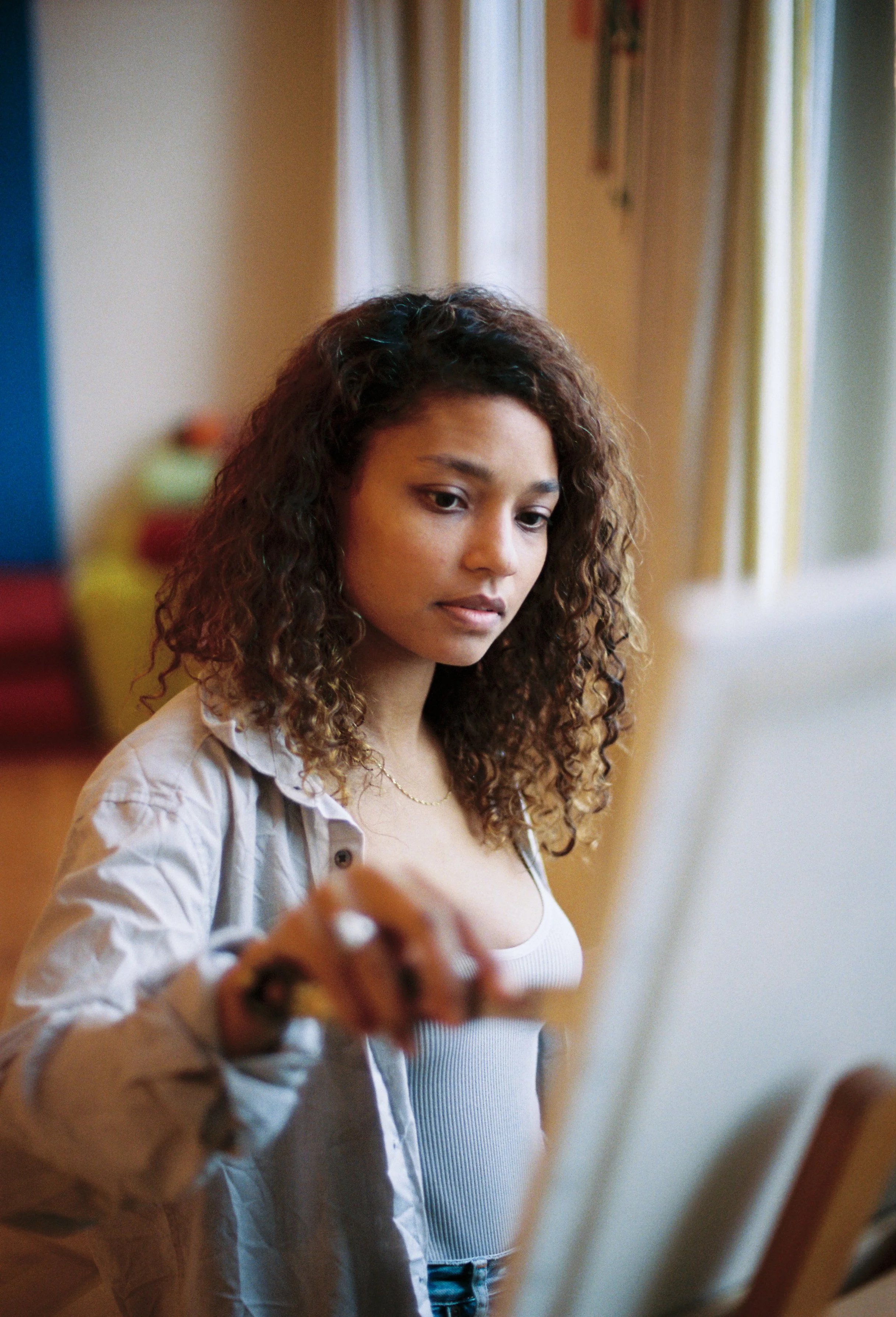 Thuli Wolf wearing a light-colored shirt over a white tank top, painting on an easel.