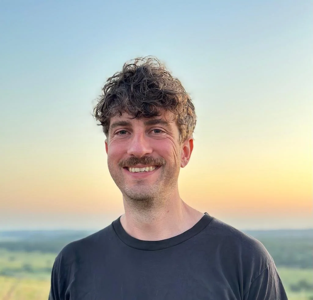 young man with mustache in a dark blue sweatshirt with a sunset in the background