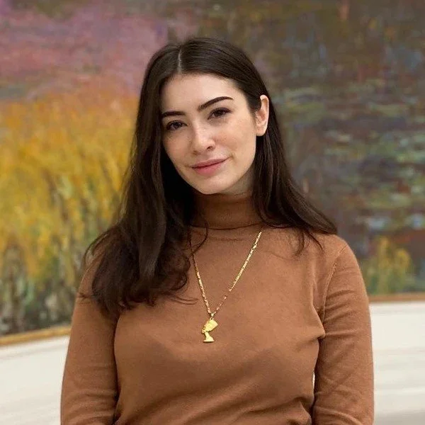 young woman in a brown turtleneck with a Monet Painting in the background