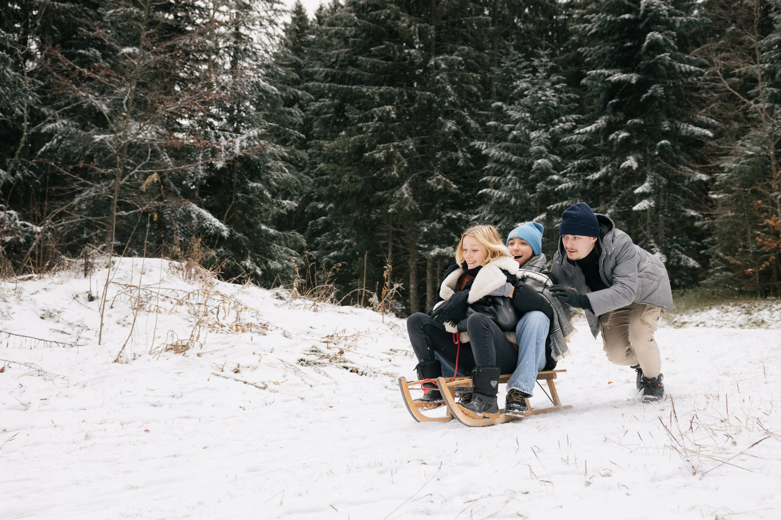 Trois personnes faisant de la luge sur de la neige dans une forêt.