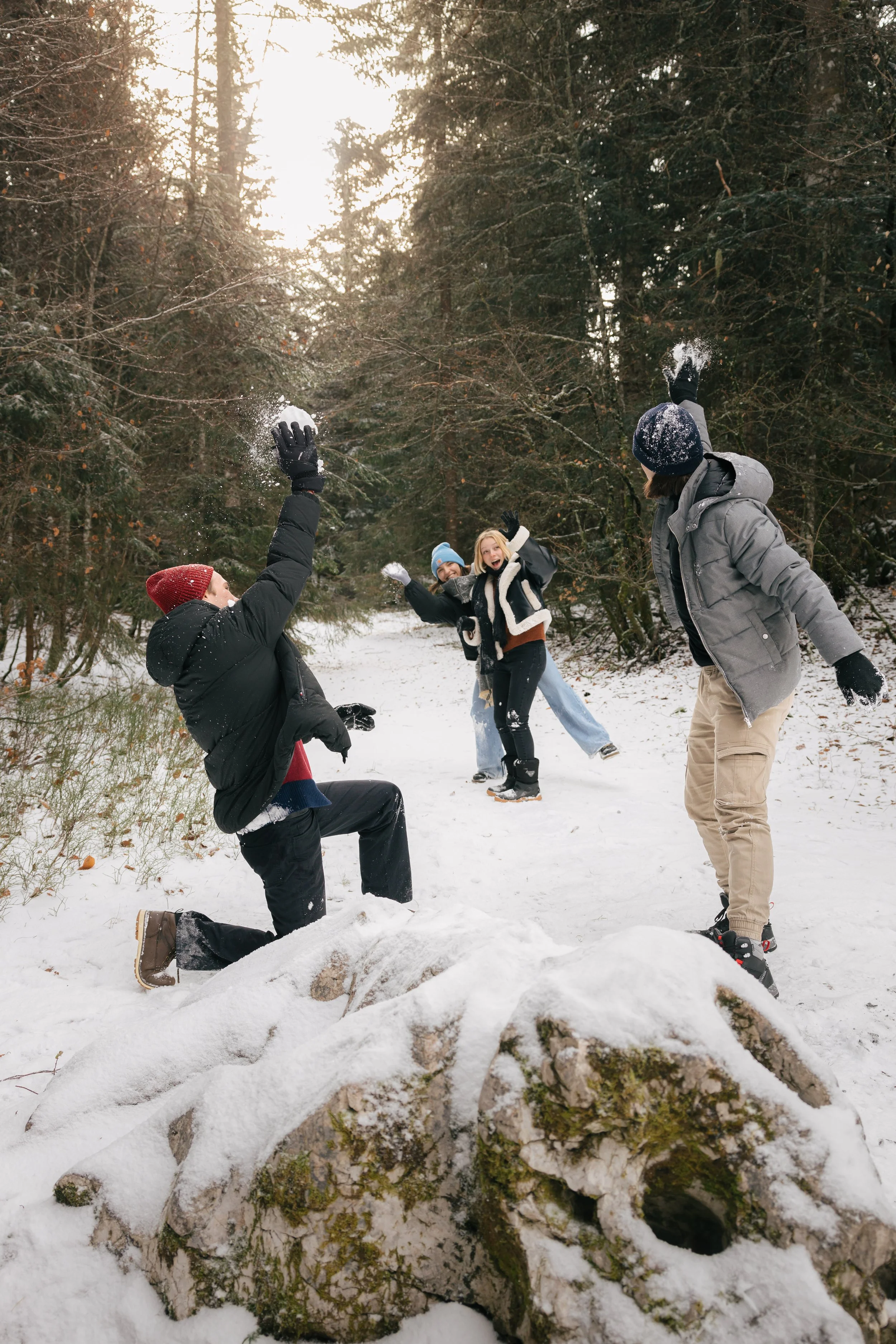 Des personnes jouent à lancer des boules de neige dans une forêt enneigée.